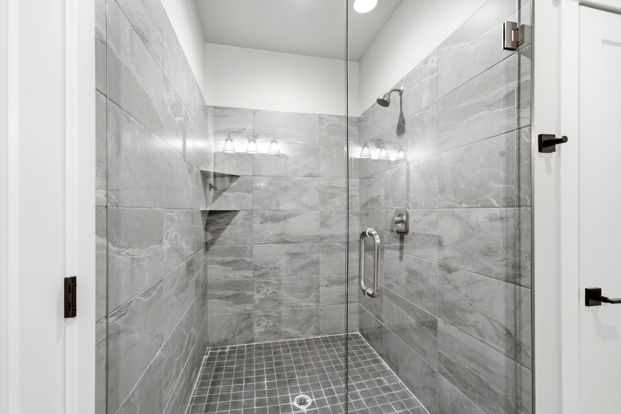 Glass-enclosed shower featuring large format gray tile walls and a mosaic tile floor