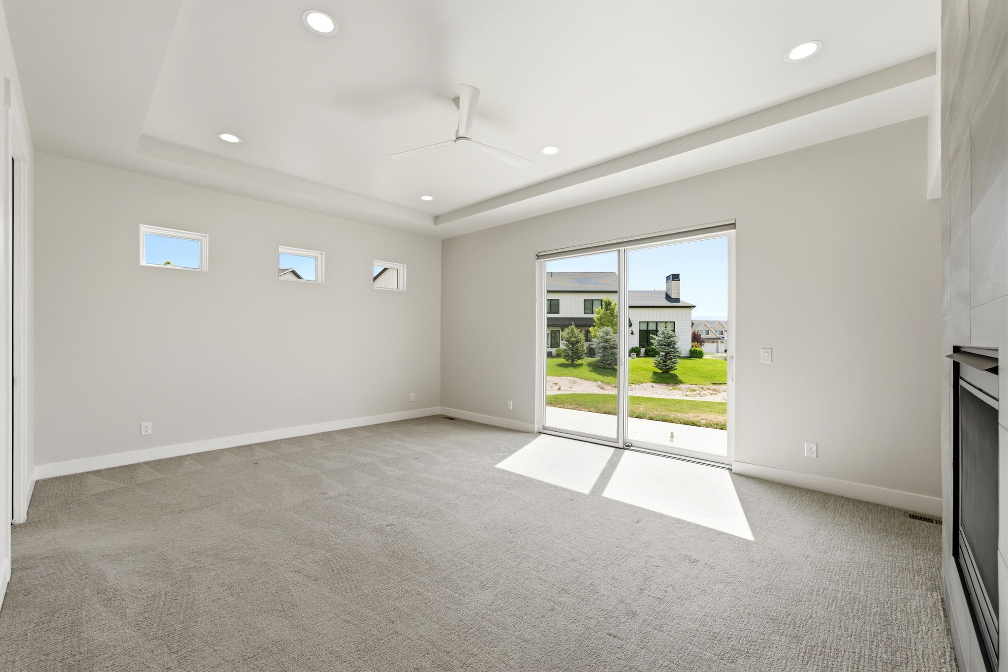 Spacious room featuring a tray ceiling with recessed lighting, a ceiling fan, and light gray wall-to-wall carpeting