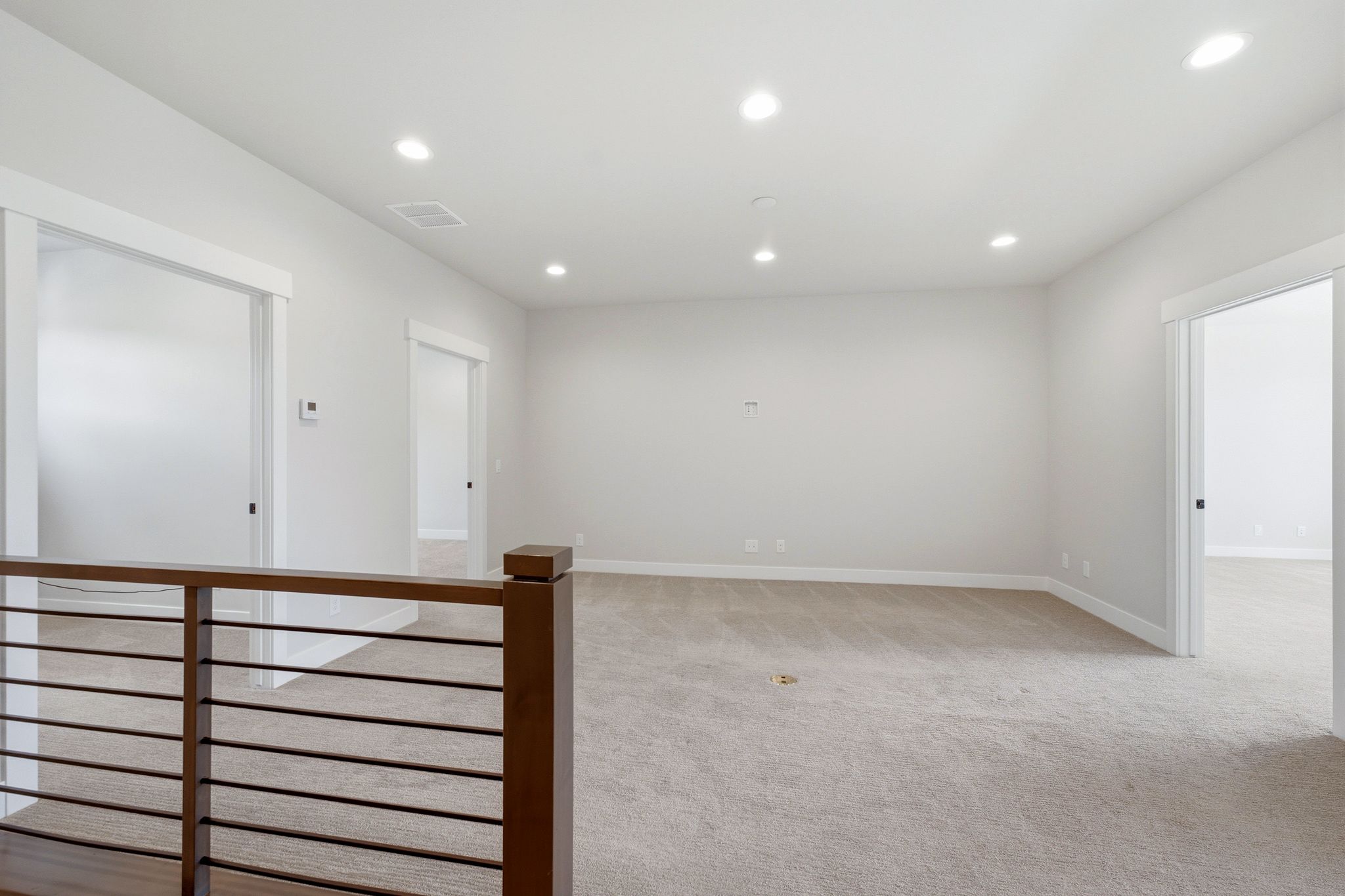 Open landing area featuring light-toned carpet, recessed ceiling lighting, and a modern wood-finish railing with horizontal balusters