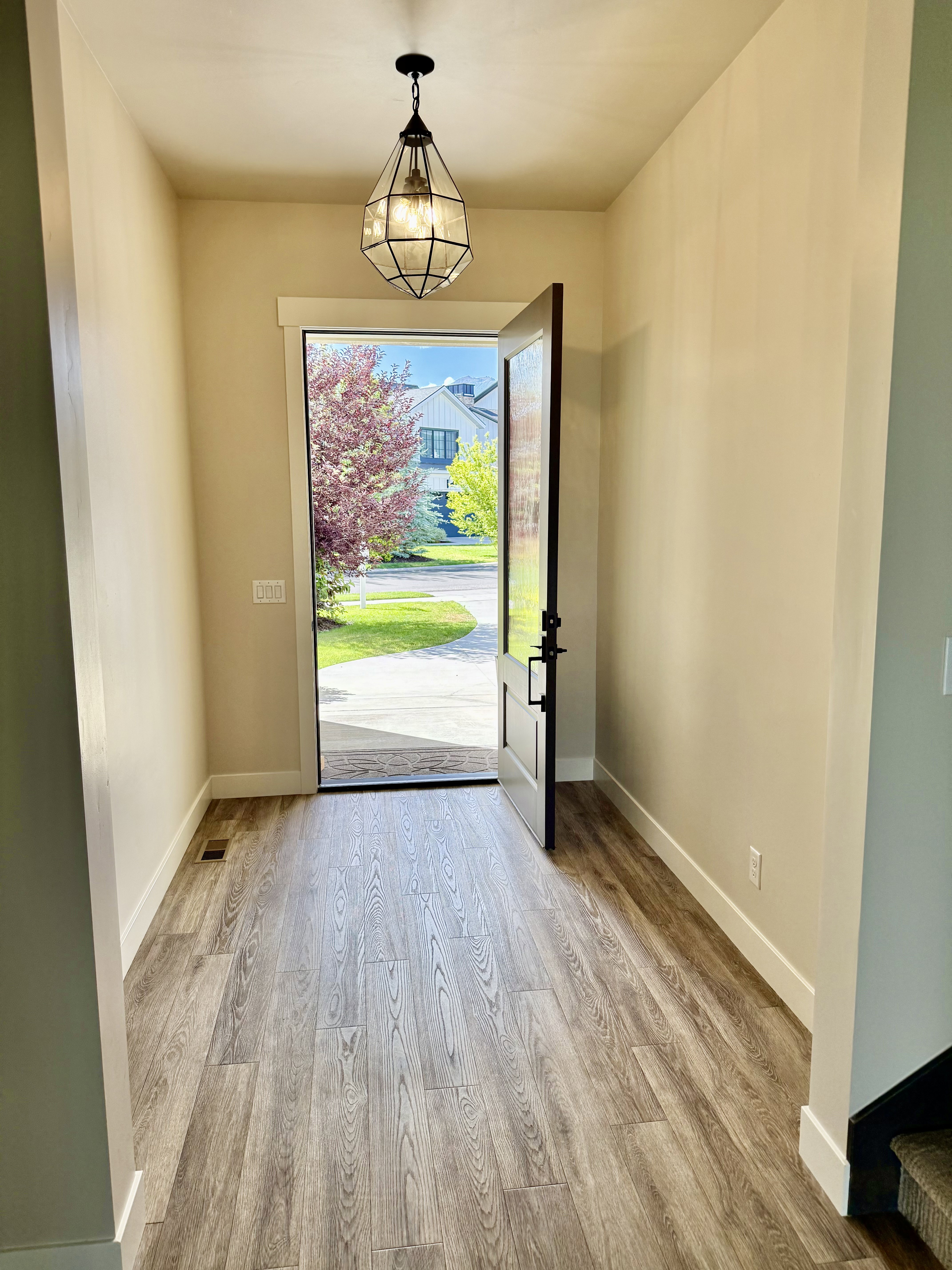 Inviting entryway featuring wood-finish flooring, a geometric pendant light fixture, and a dark-paneled front door with matte black hardware