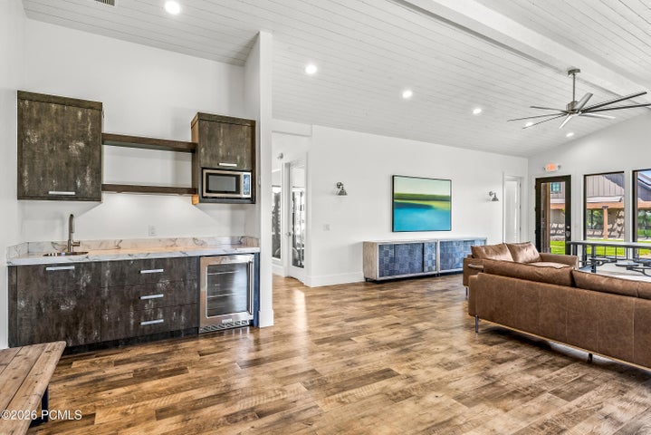 Spacious common area featuring wood-finish flooring, a vaulted ceiling with exposed beams, and a built-in wet bar with a microwave and beverage cooler
