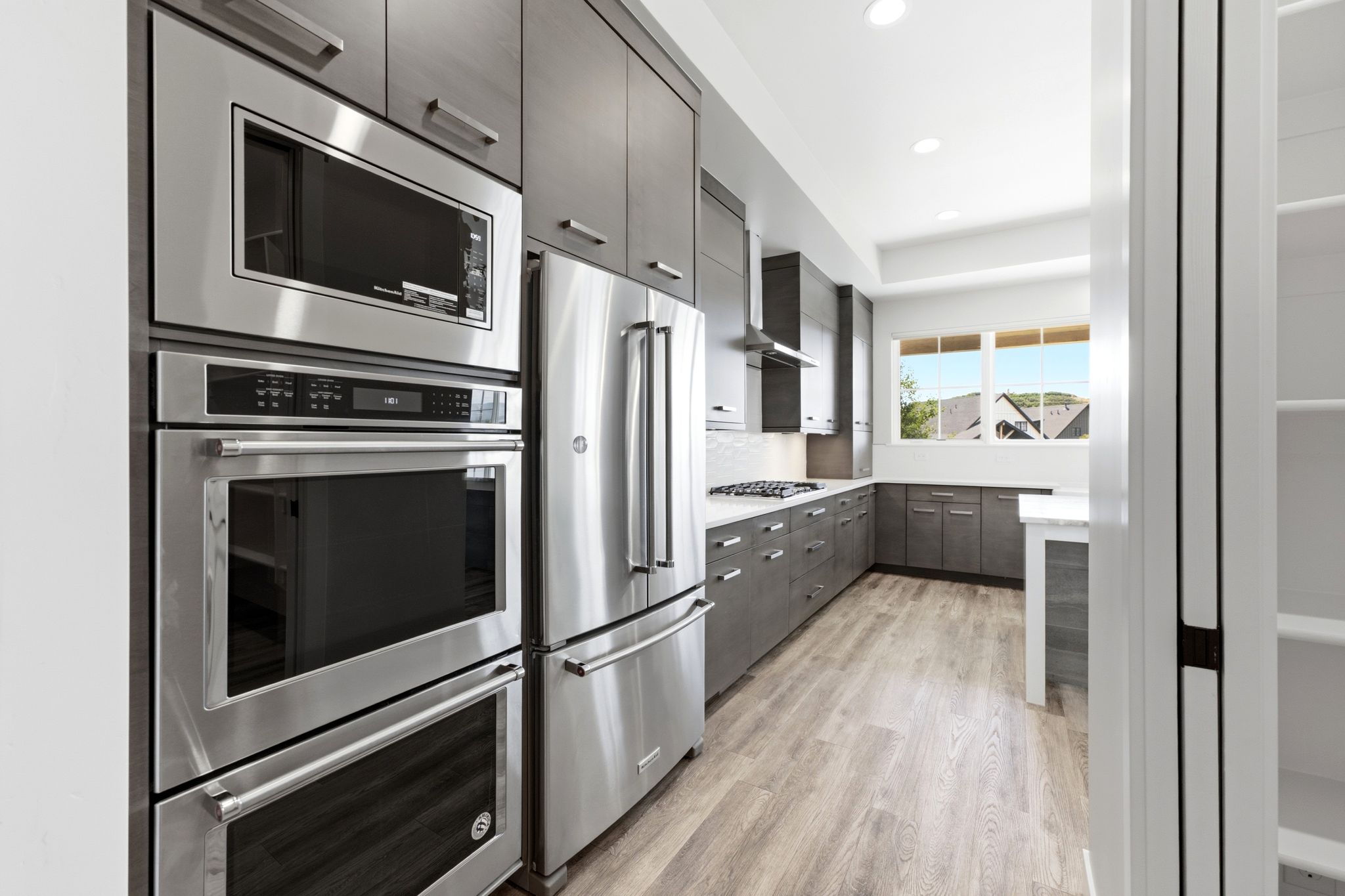 Modern kitchen featuring stainless steel appliances, dark wood-finish cabinetry, light wood-finish flooring, white countertops, and recessed lighting