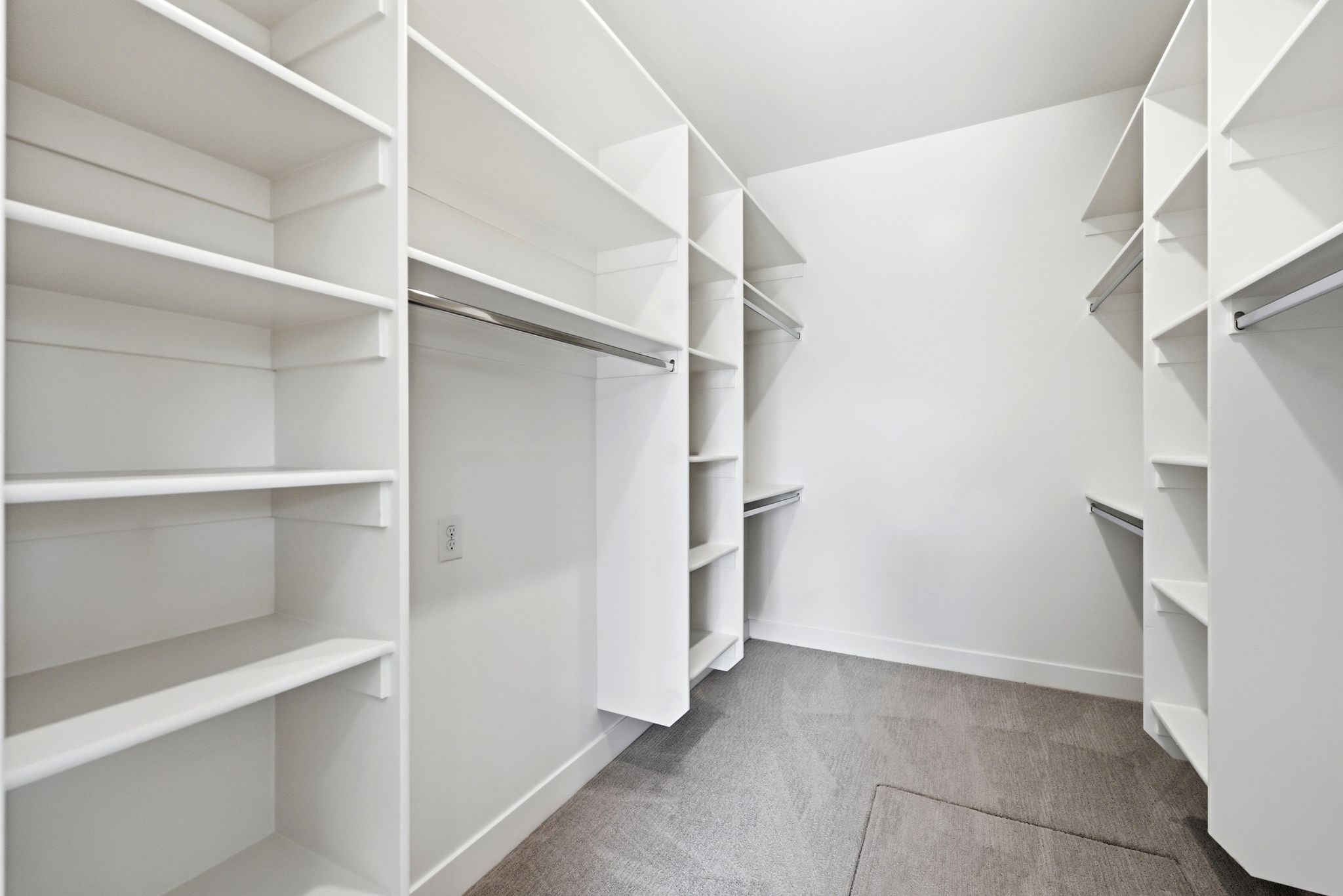 Walk-in closet featuring white built-in shelving, multiple hanging rods, and grey carpet flooring