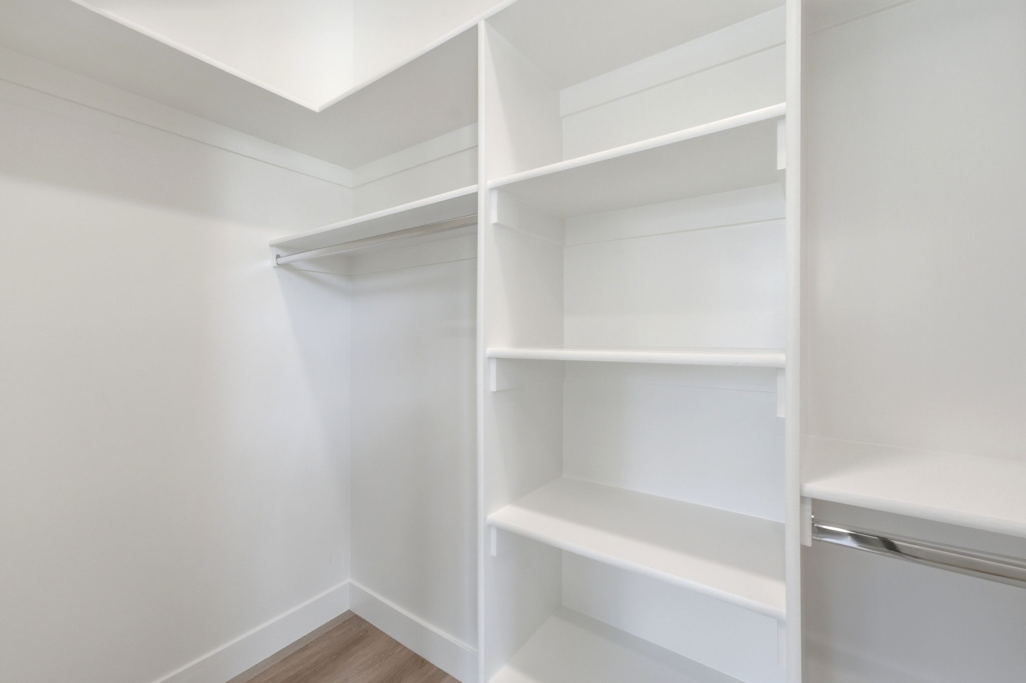 Walk-in closet featuring white built-in shelving, white walls, and wood-finish flooring