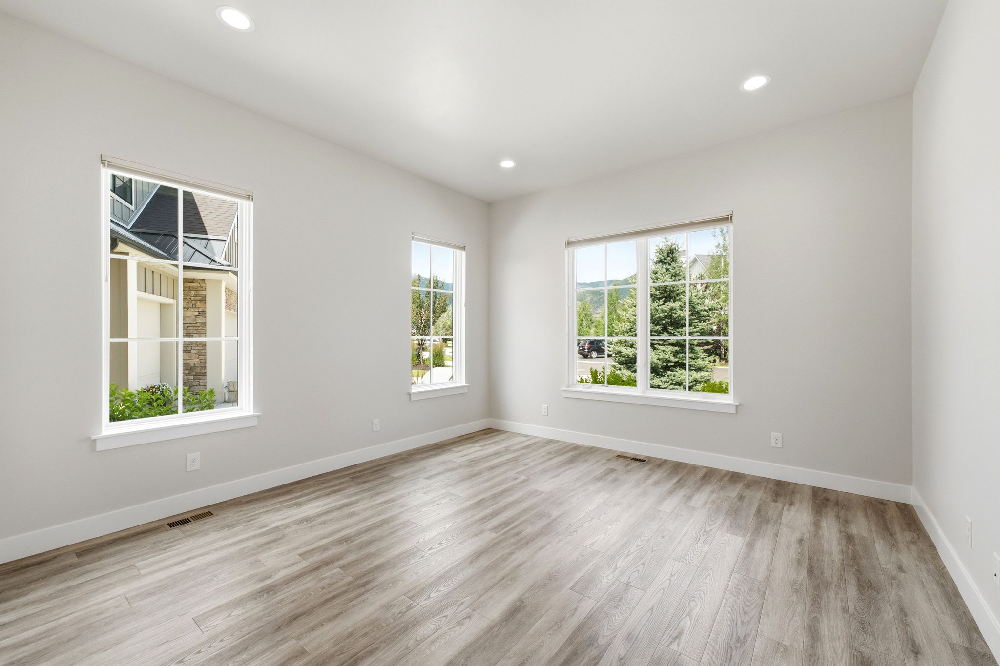 Spacious room featuring light wood-finish flooring, recessed lighting, and multiple large windows with white trim