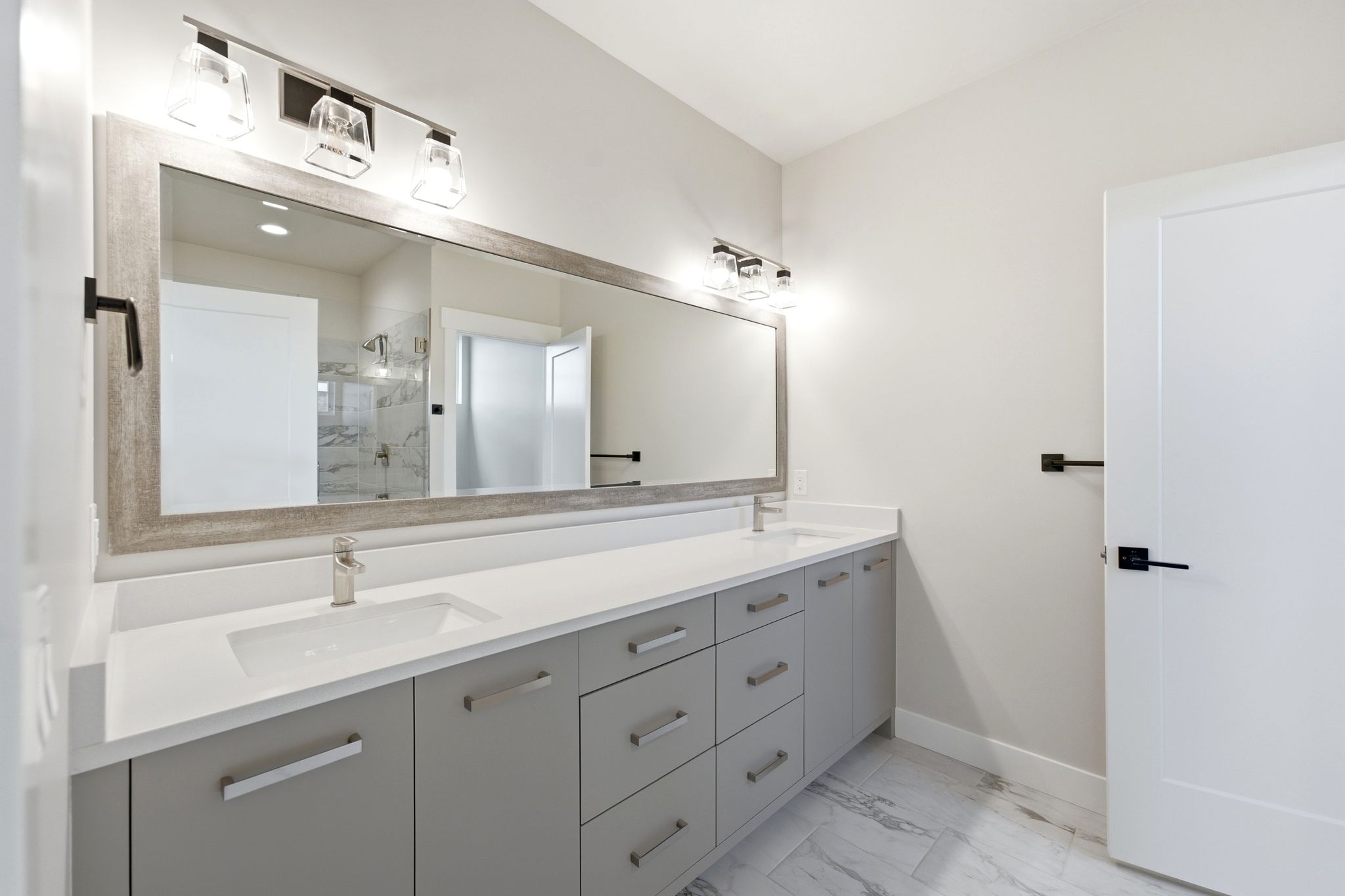 Double vanity with integrated sinks, white countertops, gray cabinetry, brushed nickel hardware, and wood-finish framed mirror