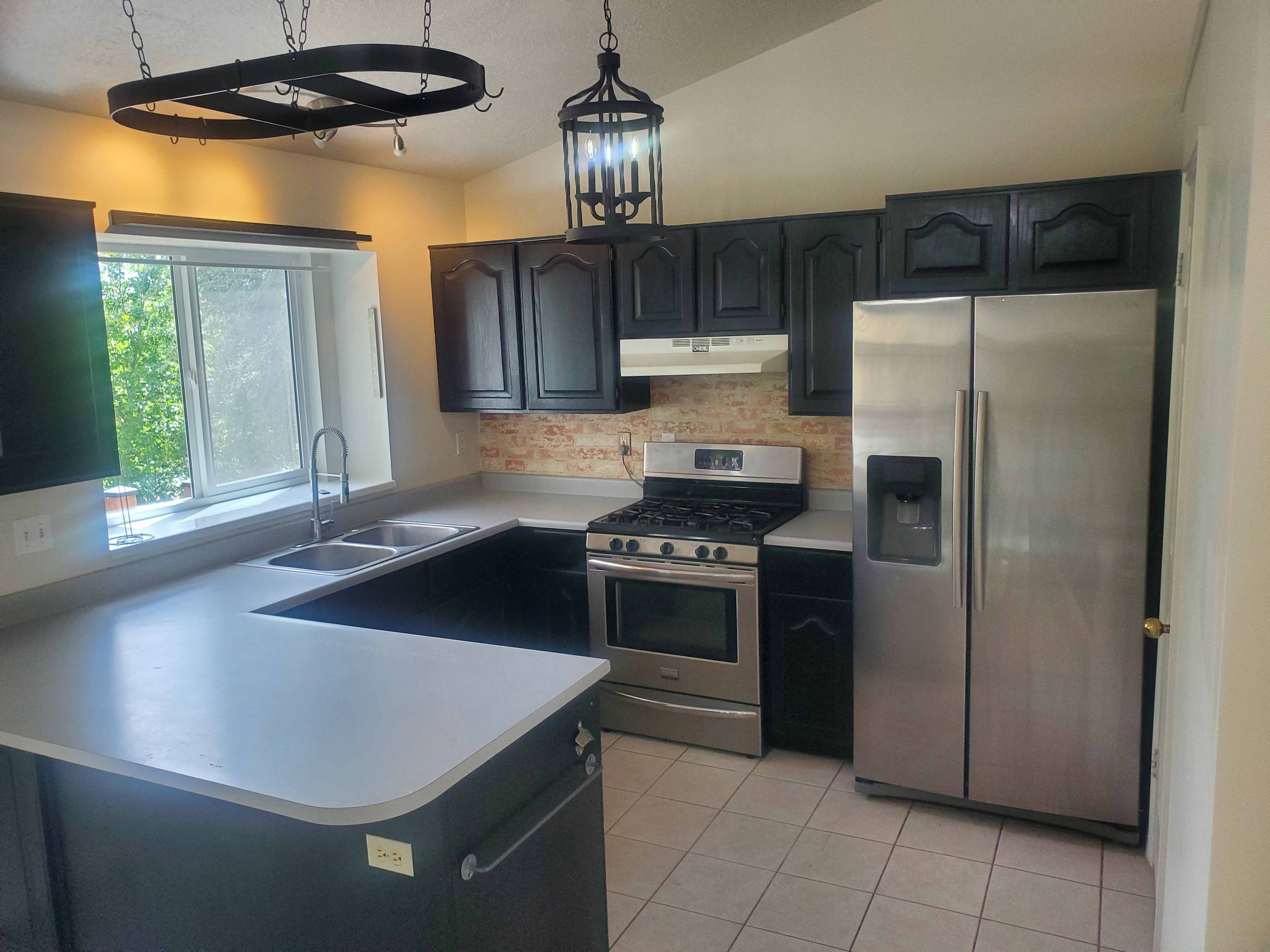 Kitchen featuring dark cabinetry, light countertops, stainless steel appliances, a double basin sink, and tile flooring