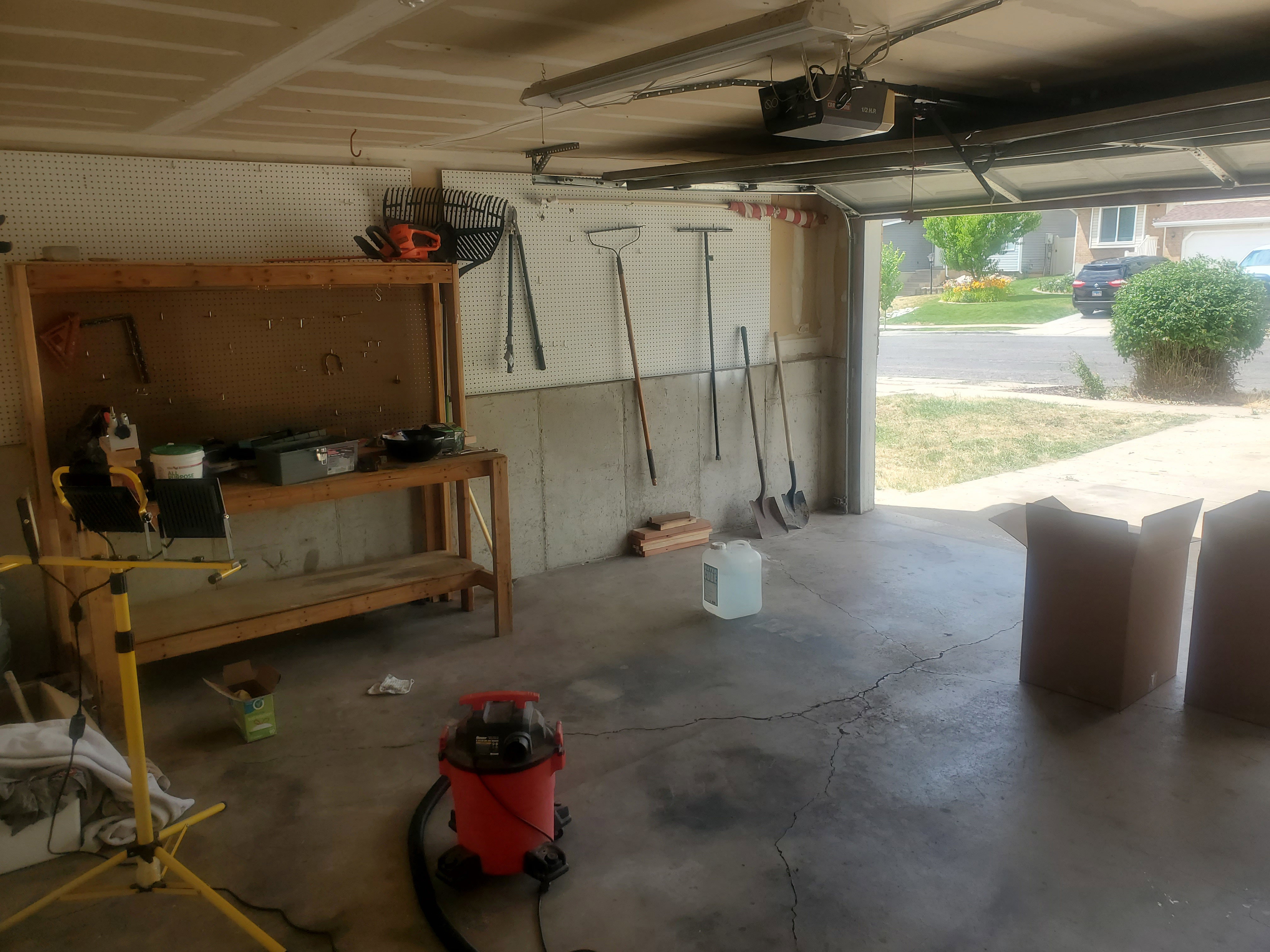 Garage interior featuring a concrete floor, exposed ceiling joists, and a built-in workbench with pegboard storage