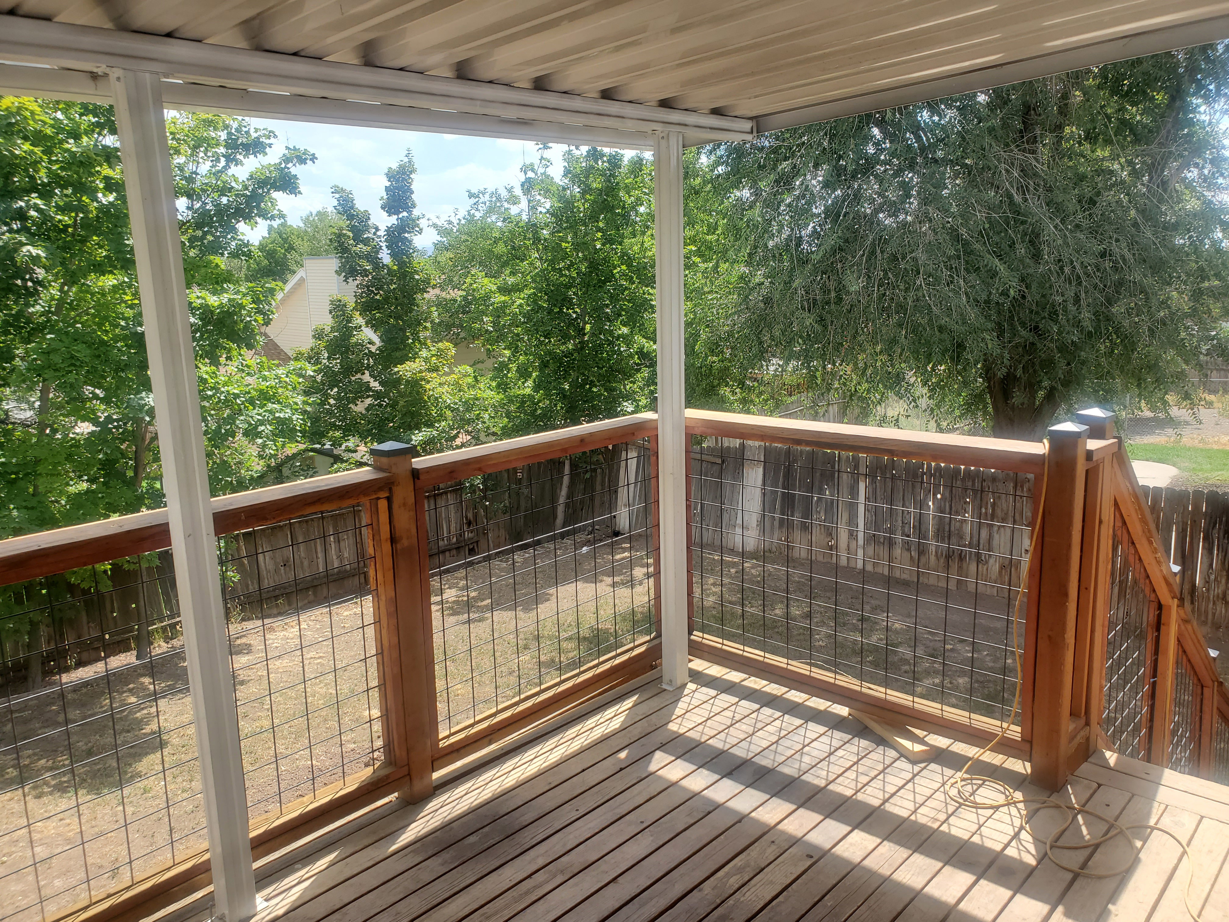Covered exterior deck featuring wood plank flooring, wood and wire railing, and a corrugated metal roof
