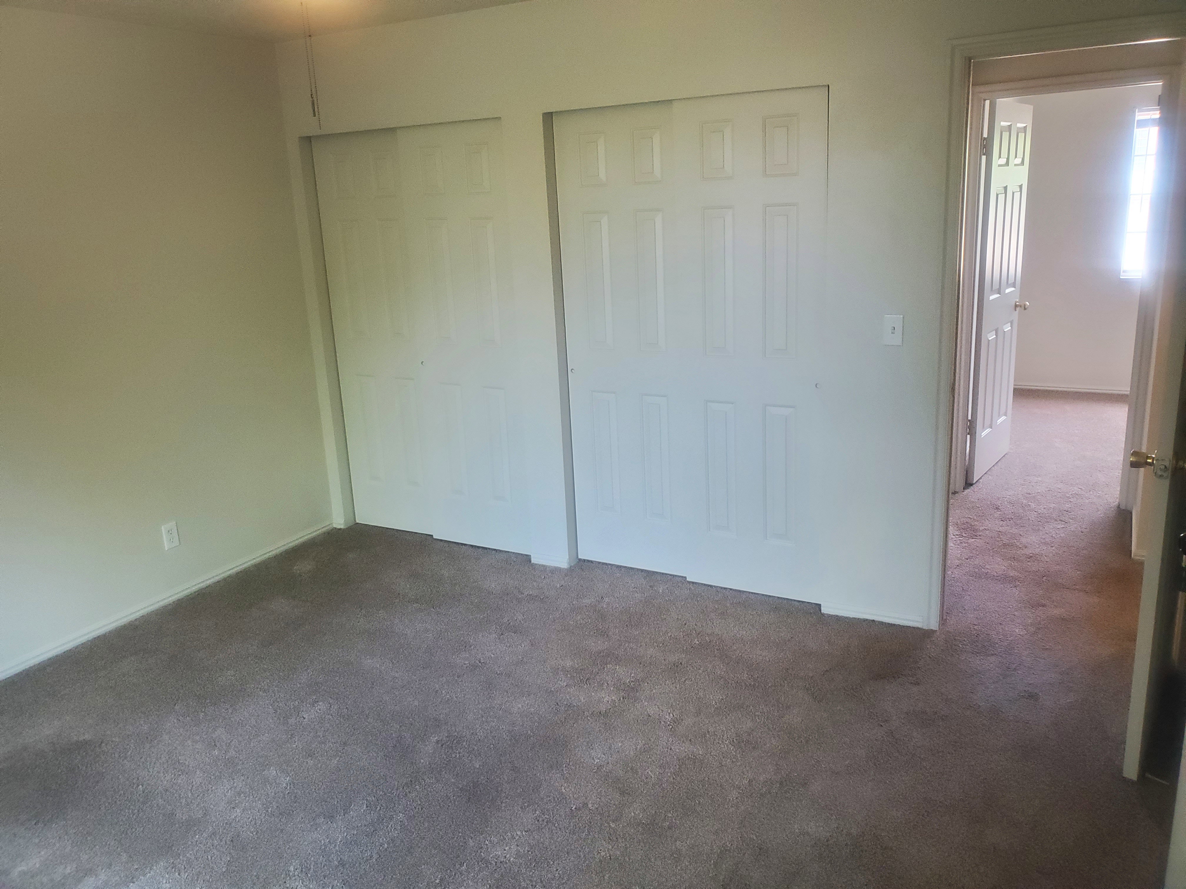 Interior room featuring neutral wall paint, gray carpet, and two sets of bi-fold closet doors