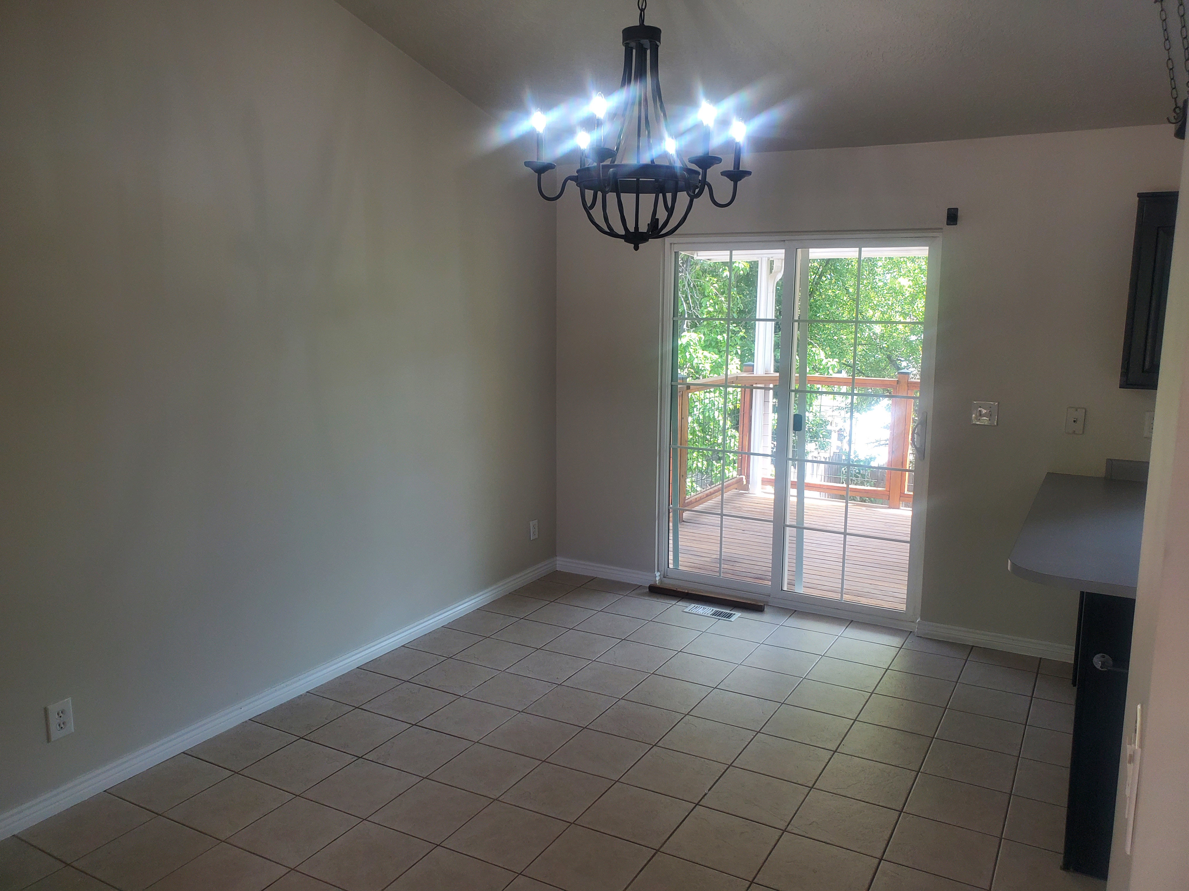 Dining area with tiled flooring, a black chandelier, and sliding glass doors opening to an exterior wood deck