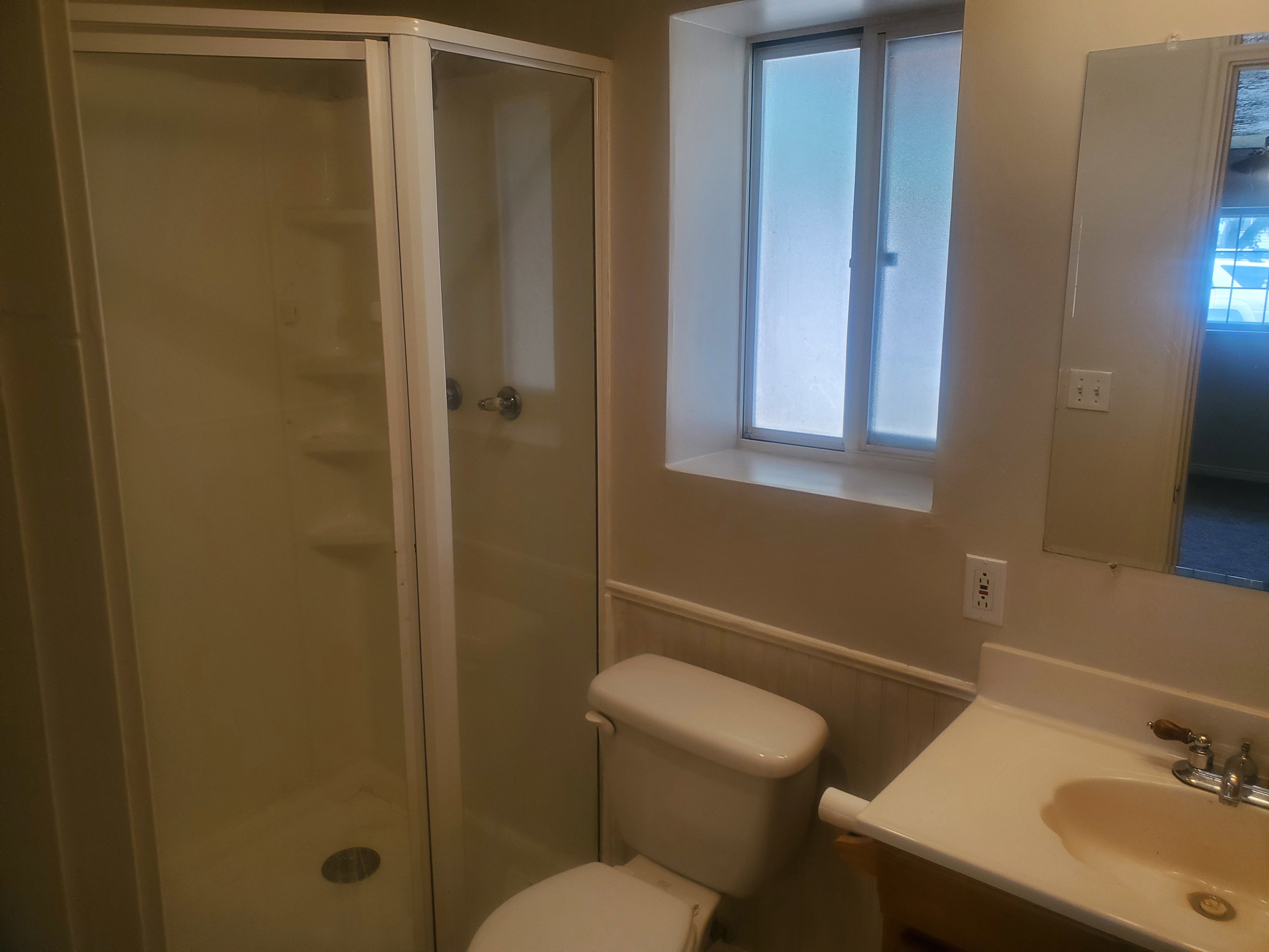 Corner shower enclosure with clear glass doors, white shower base, and integrated shelving