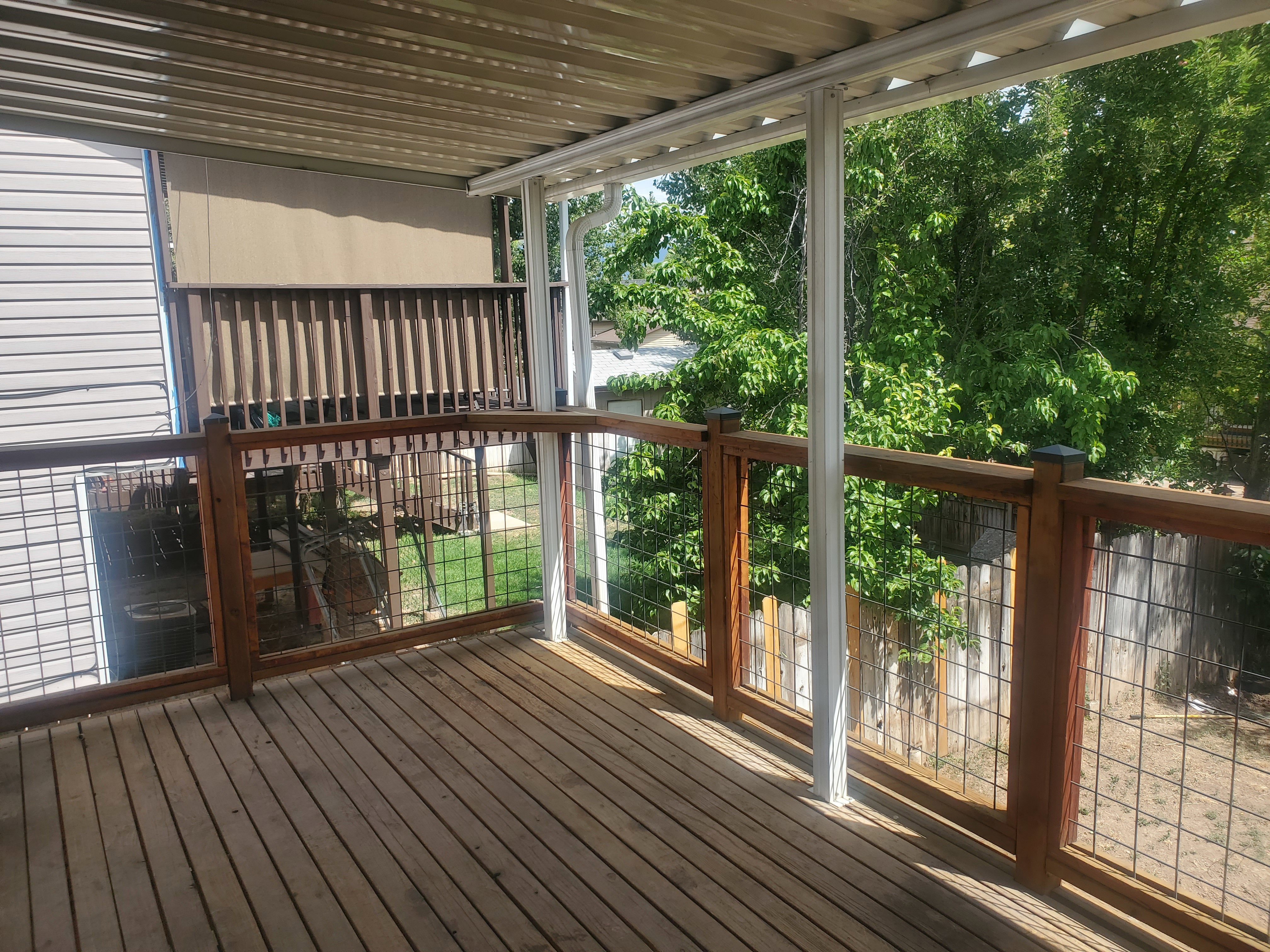 Covered deck featuring wood decking, wood and wire railing, and a corrugated metal roof