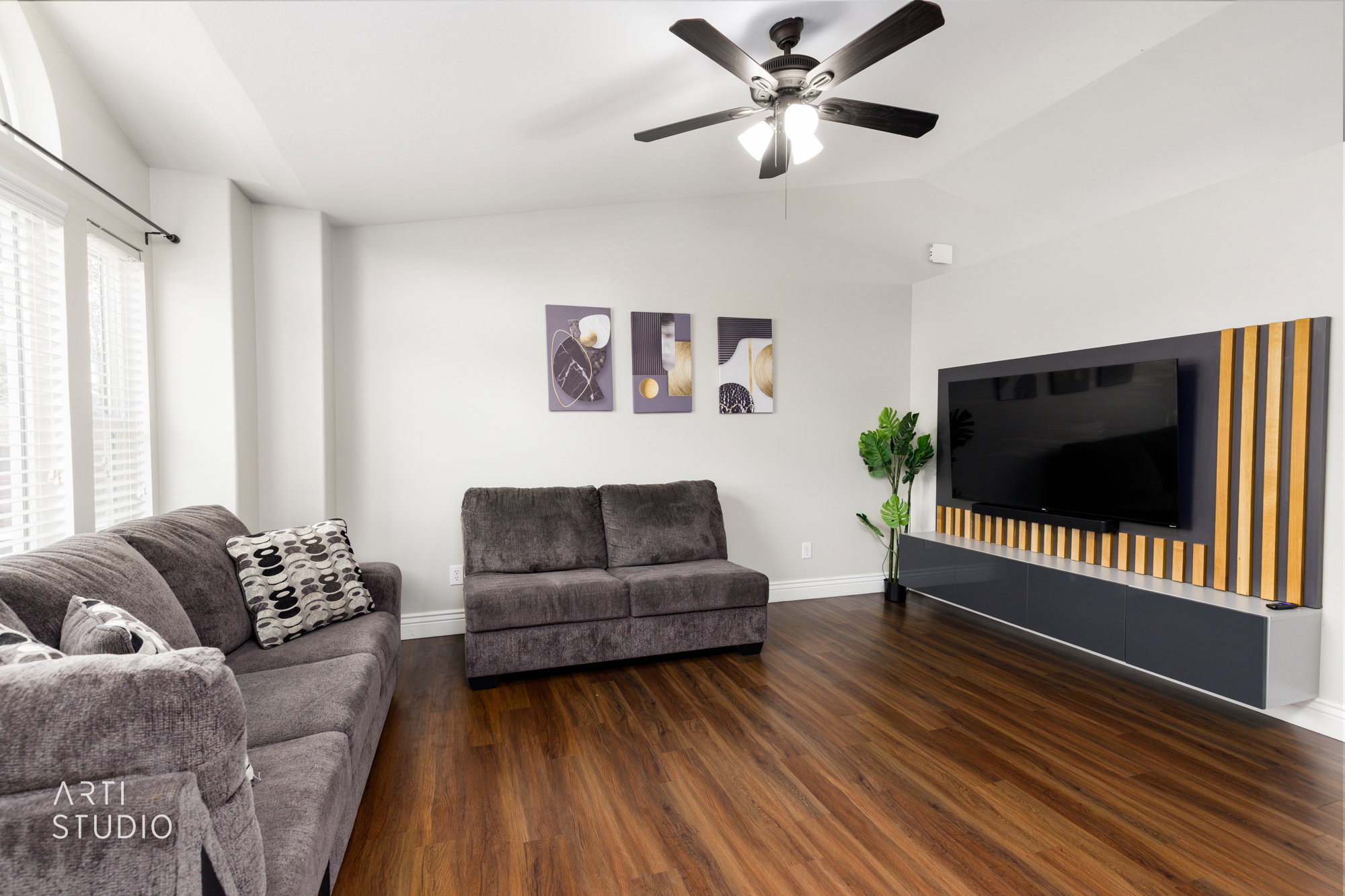 Living area featuring wood-finish flooring, a contemporary ceiling fan, and a built-in media console with vertical wood slat detailing