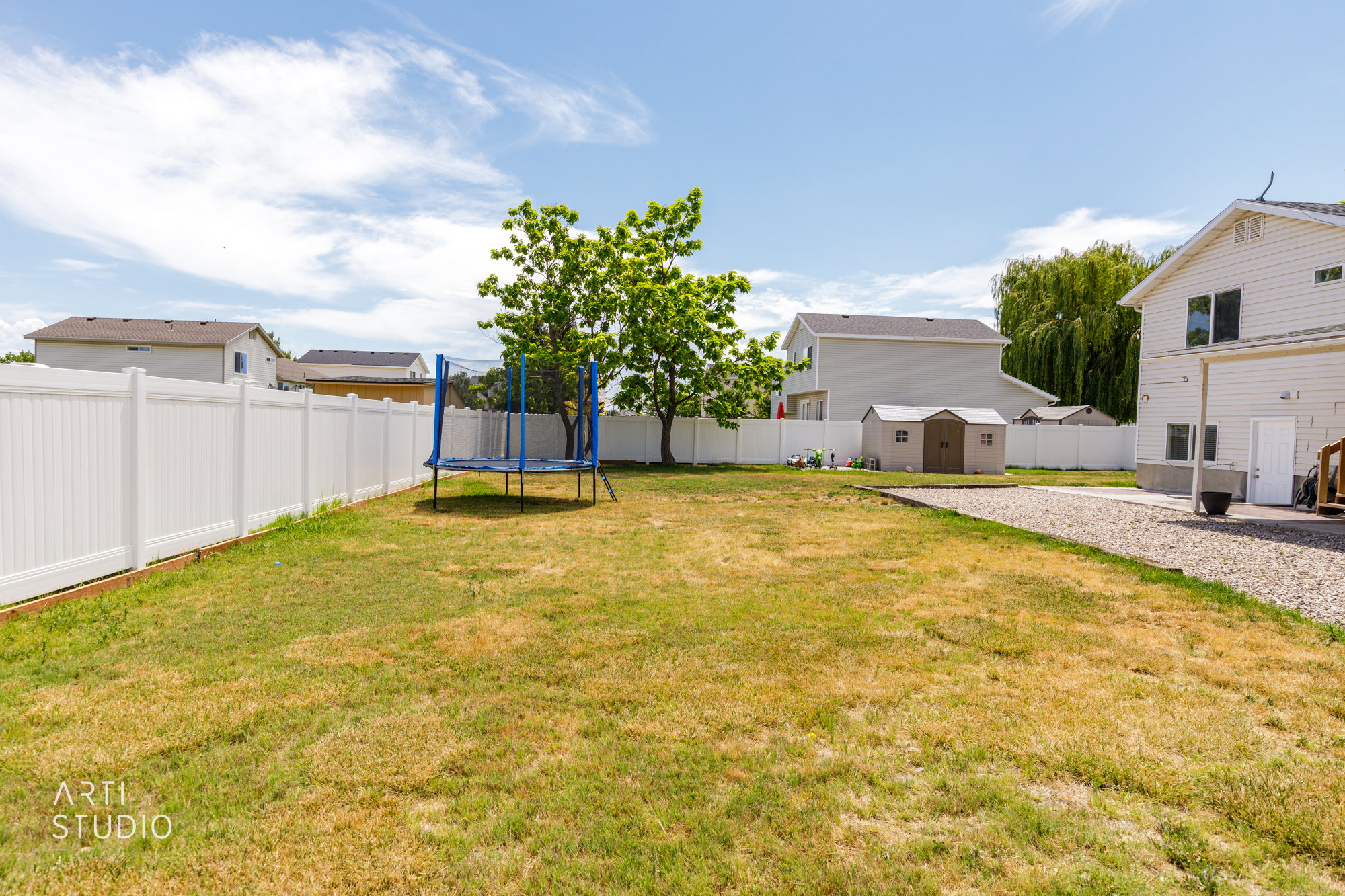 Expansive backyard featuring a white vinyl fence, gravel patio area, and mature trees