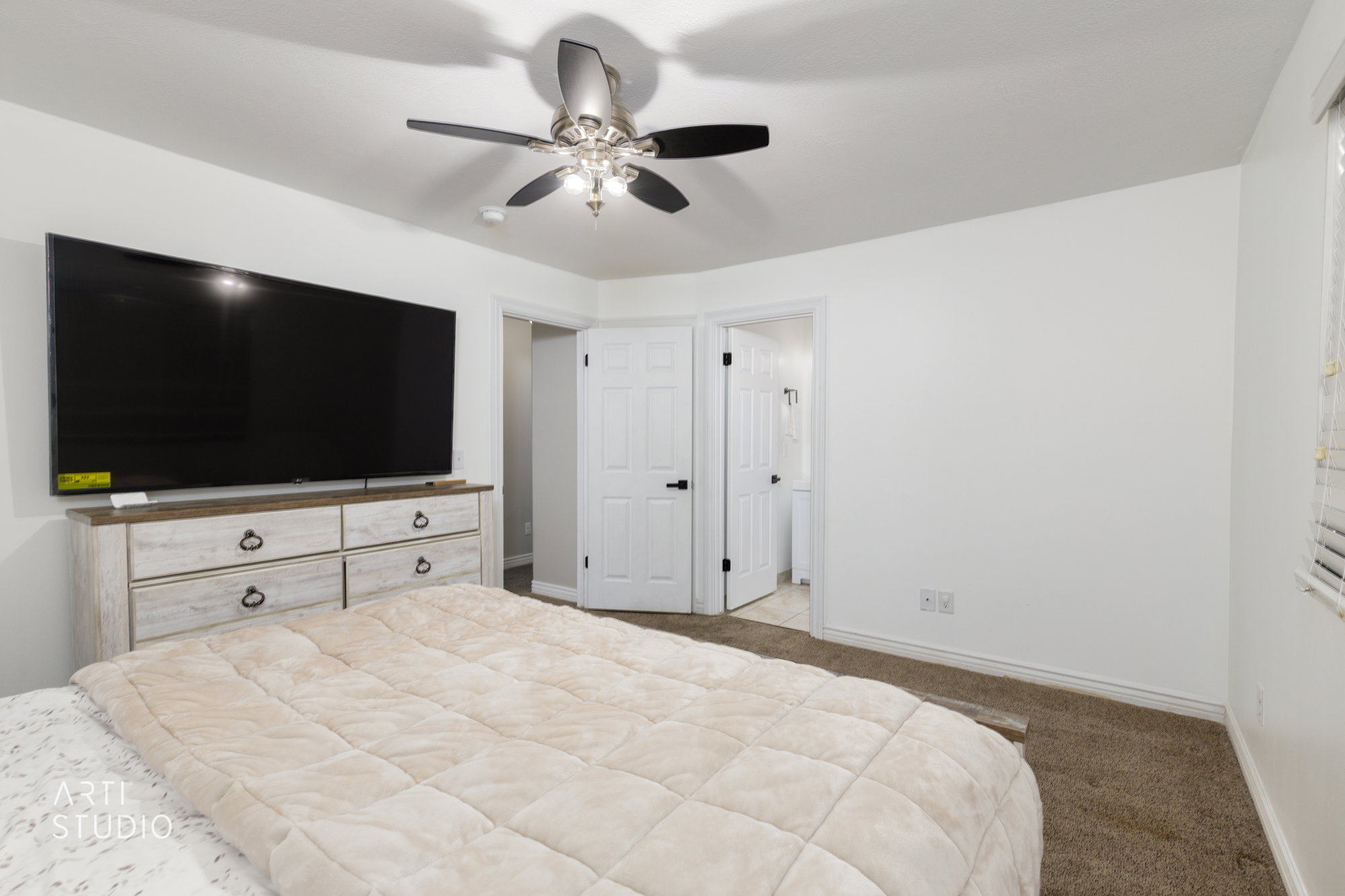 Bedroom space featuring a ceiling fan with integrated lighting, a neutral color palette, carpet flooring, and white interior doors with black hardware