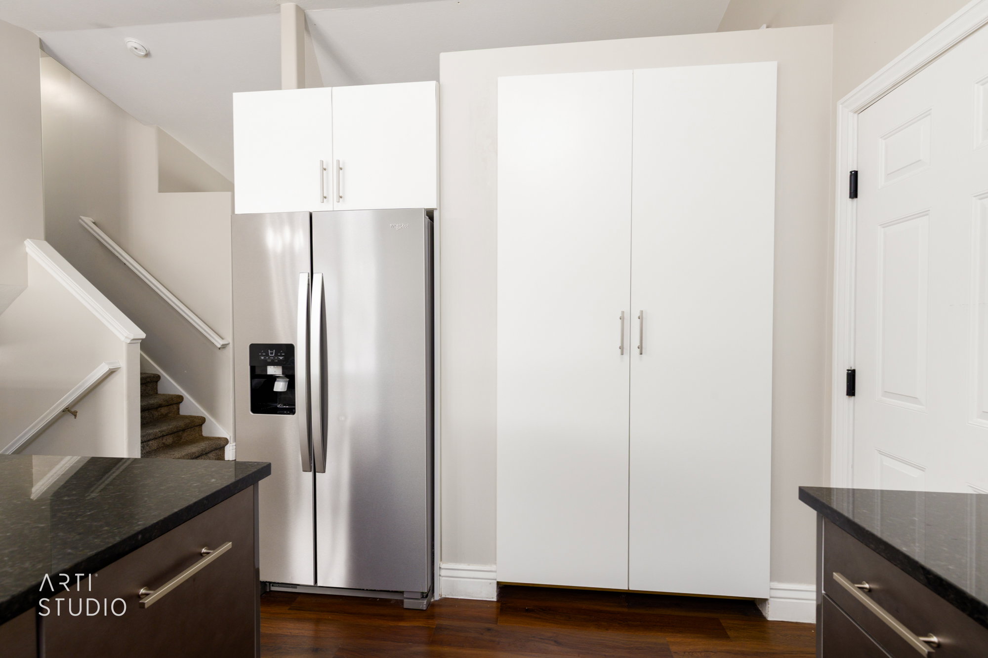 Stainless steel refrigerator with a built-in dispenser, complemented by white upper cabinetry and a tall white pantry cabinet