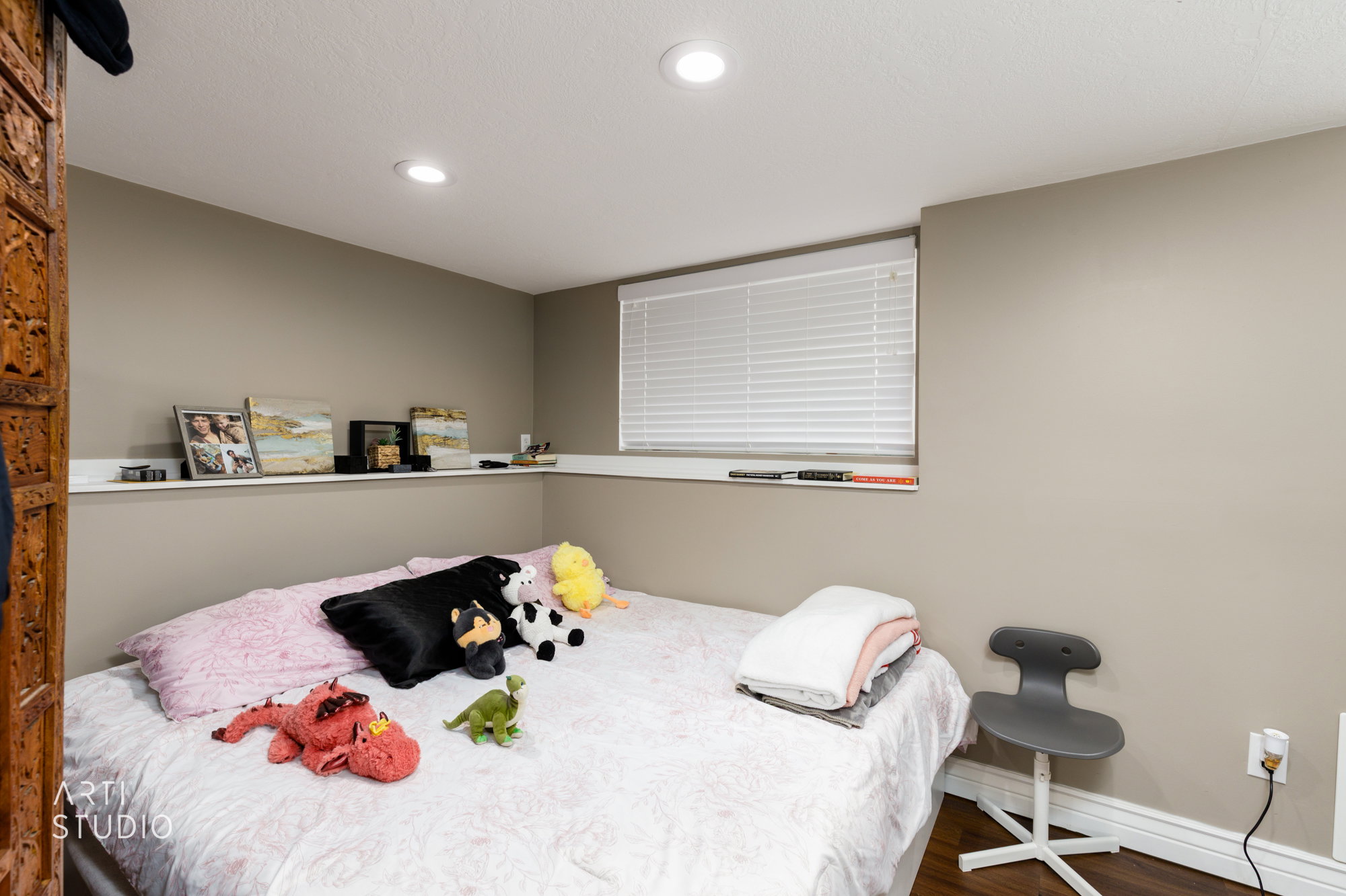 Recessed ceiling lighting illuminates a room featuring a window with horizontal blinds, neutral wall tones, and wood-finish flooring