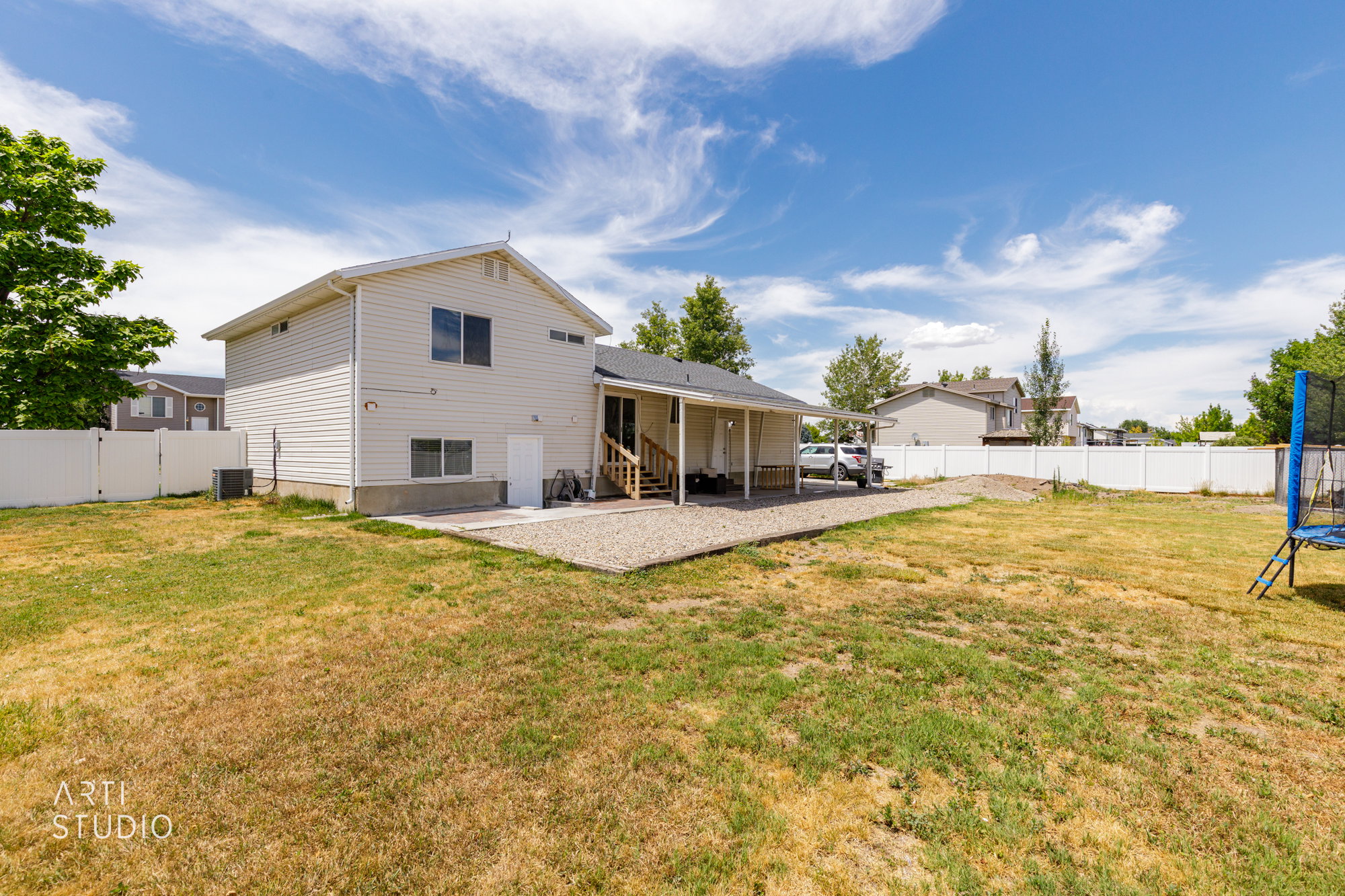 Expansive backyard featuring a white vinyl privacy fence, a concrete patio, and a covered gravel area