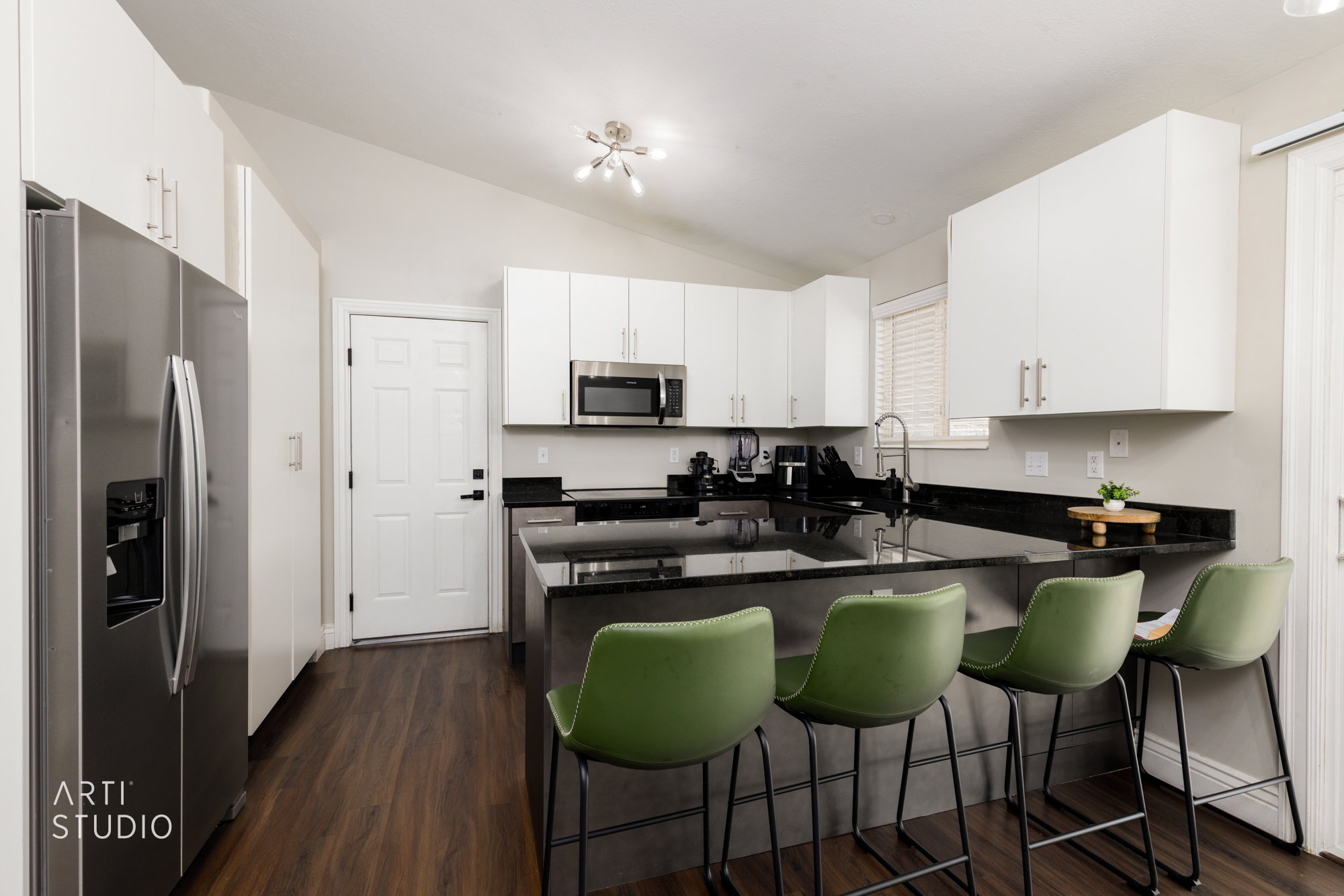 Kitchen featuring an island with seating, dark countertops, white upper and lower cabinetry, stainless steel appliances, and wood-finish flooring