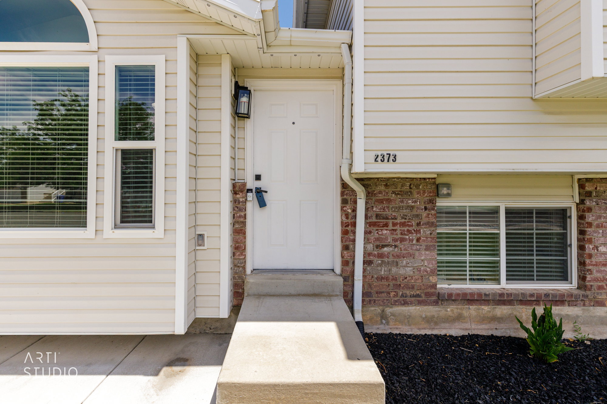 Exterior facade featuring light-colored horizontal siding, brick accents, and a prominent white entry door
