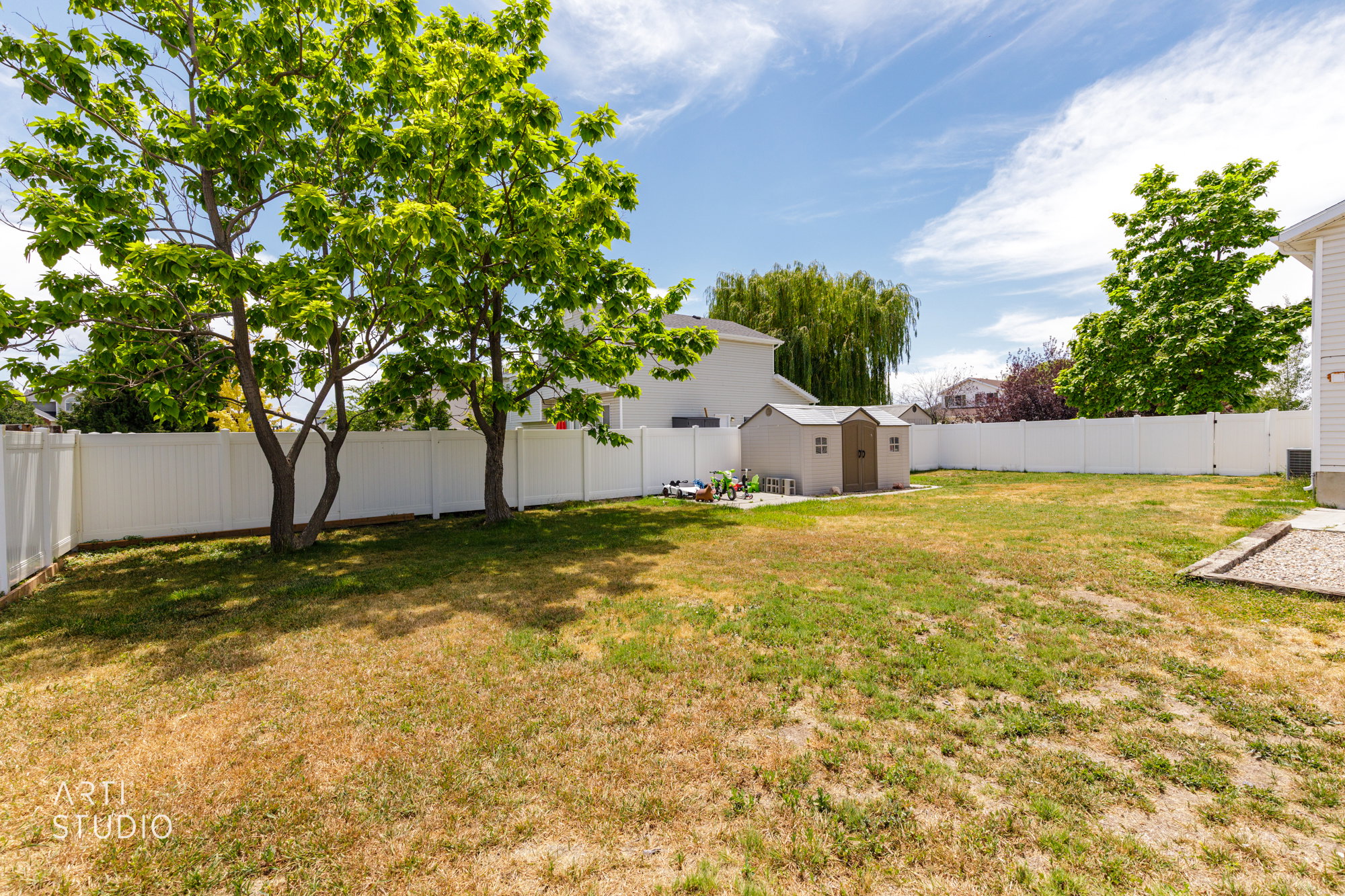 Expansive backyard featuring a white vinyl privacy fence, mature shade trees, and a utility shed