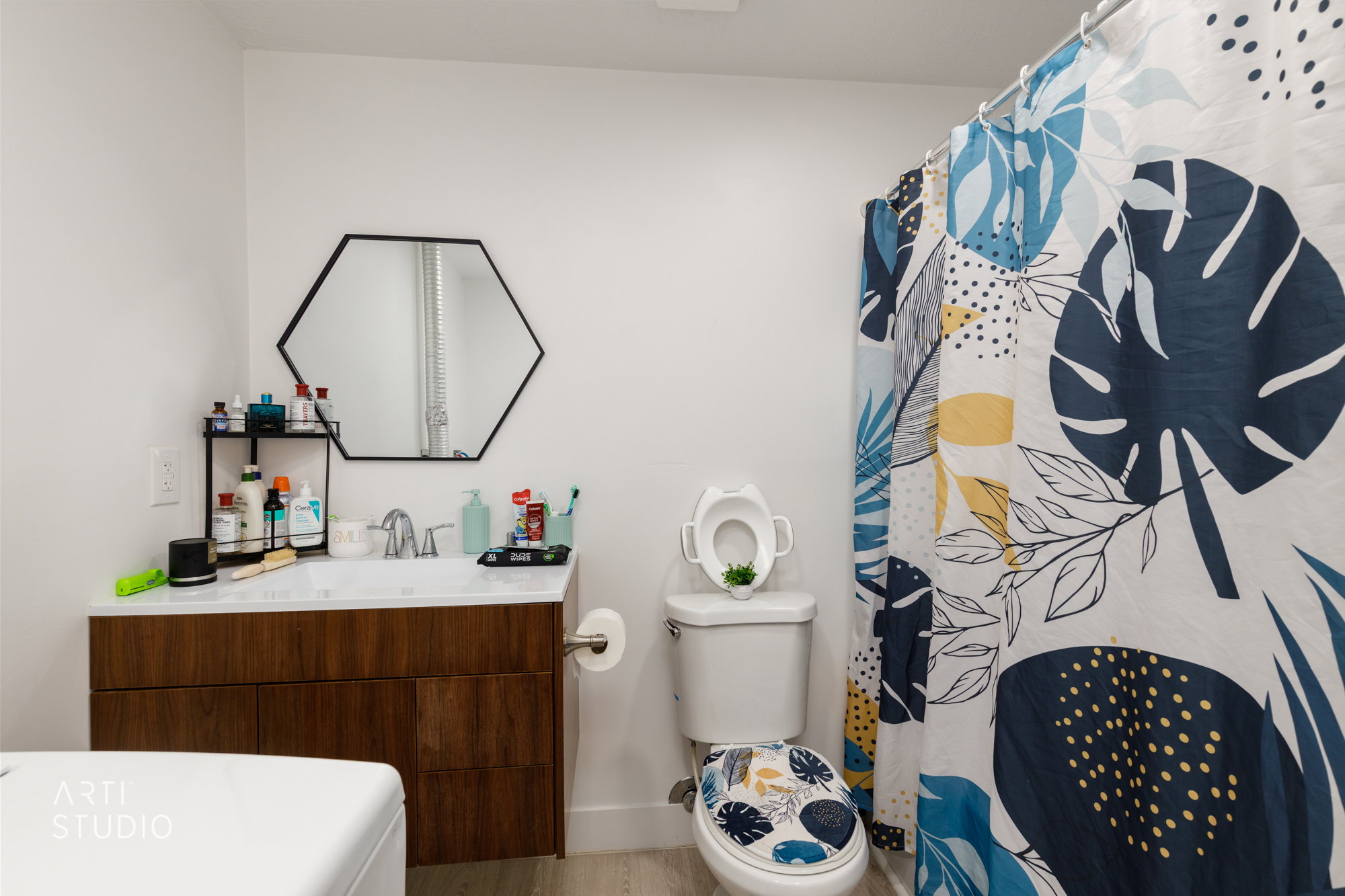 Bathroom featuring a modern wood-finish vanity with an integrated sink, hexagonal mirror, and light-tone flooring