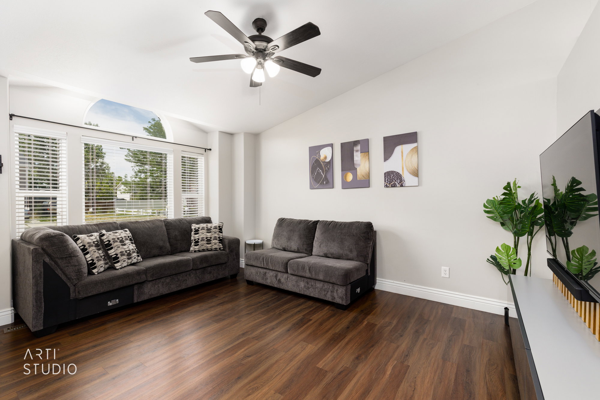 Living area featuring rich wood-finish flooring, vaulted ceilings, and a ceiling fan with integrated lighting