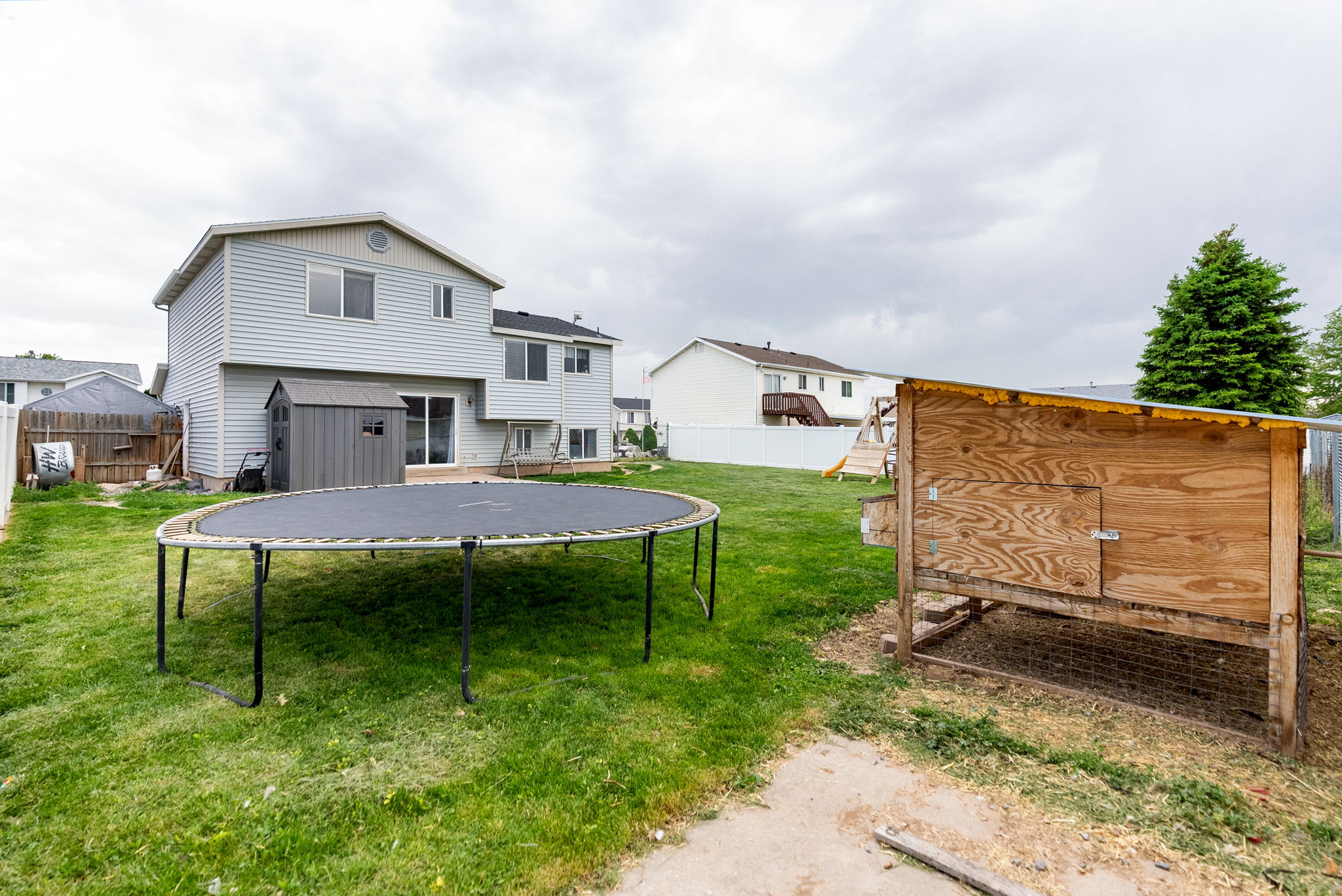 Expansive rear yard featuring green lawn, a light blue vinyl-sided dwelling, and a wood storage shed