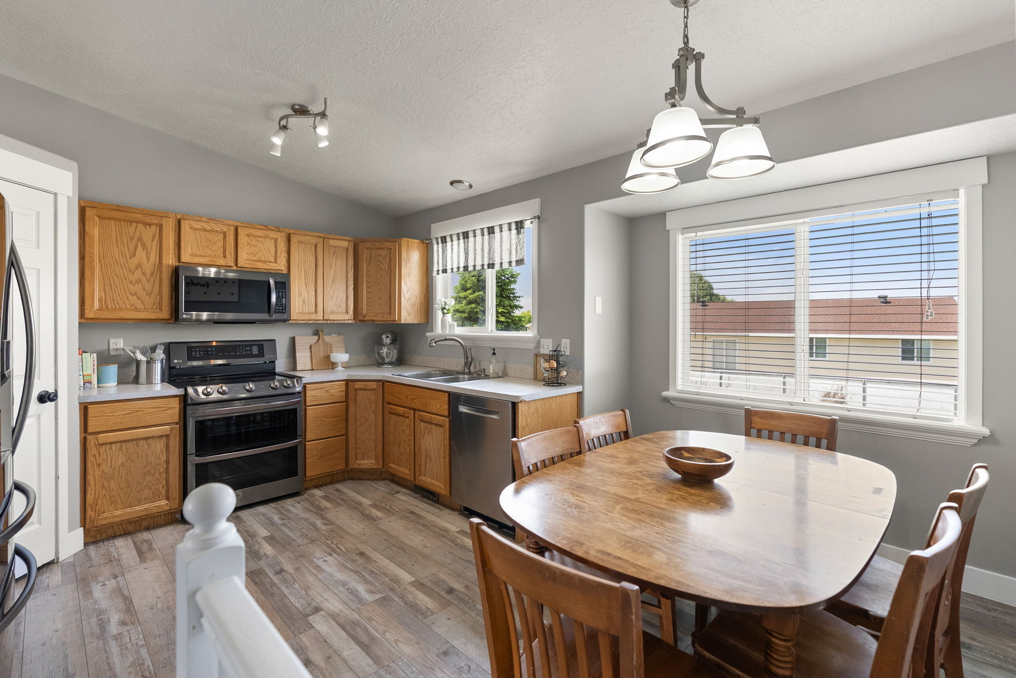 Kitchen featuring wood-finish flooring, light wood cabinetry, stainless steel appliances, and a dining area with a multi-light chandelier
