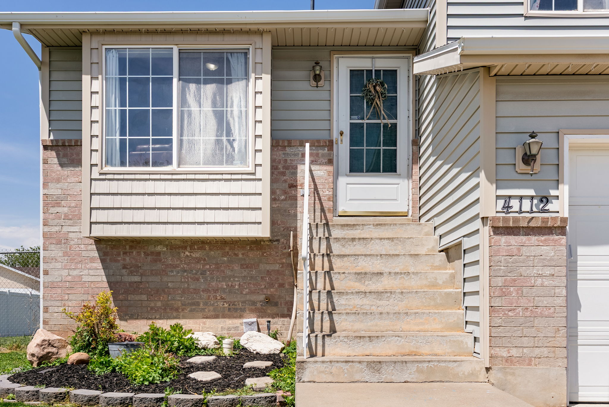 Exterior featuring a bay window with grid-patterned panes, brick and horizontal siding, a white front door with glass inserts, and a concrete staircase with a metal handrail