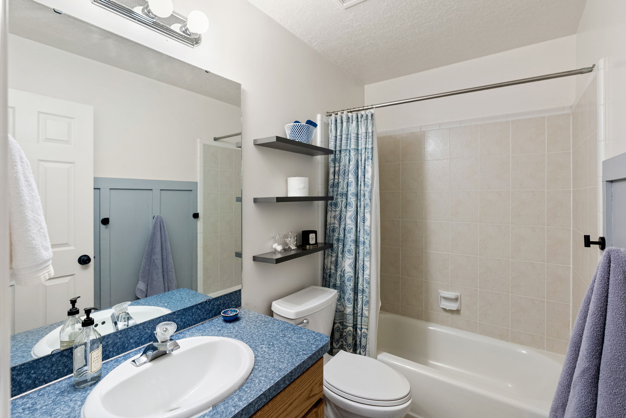 Bathroom featuring a white bathtub, ceramic tile shower surround, and a vanity with a blue speckled countertop