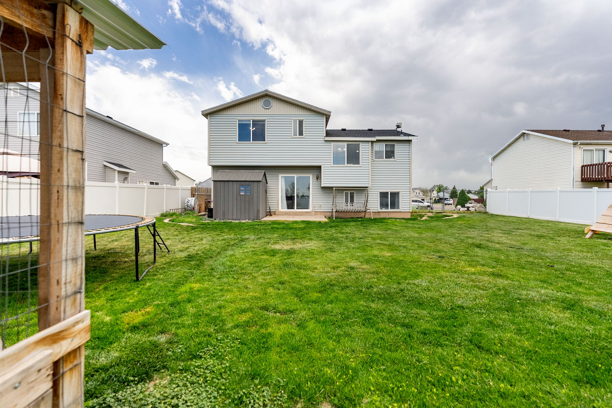Spacious backyard featuring a light-colored siding exterior, ground-level patio, built-in storage shed, and white privacy fencing