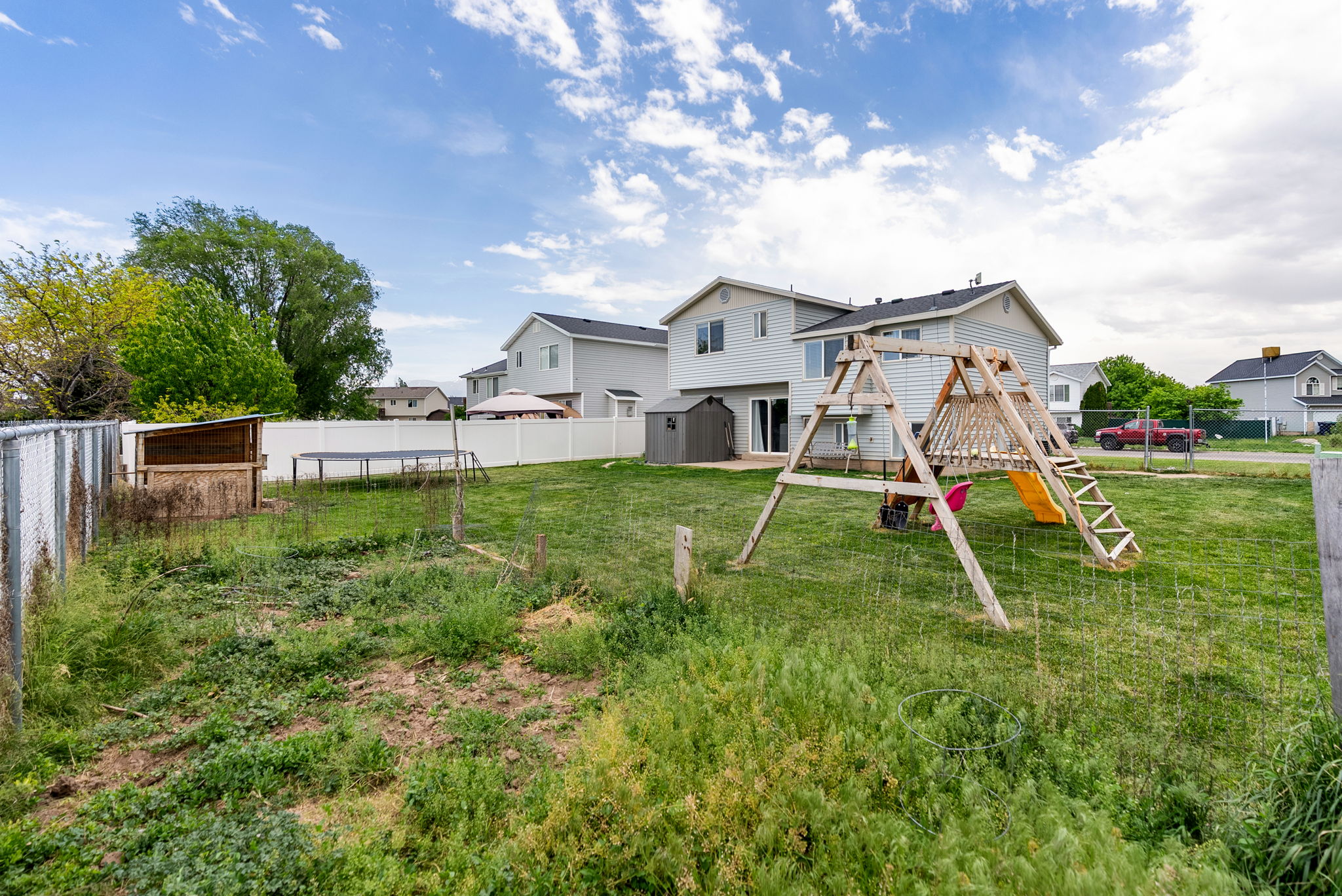 Expansive rear yard featuring chain link and vinyl fencing, a shed, and a two-story residence with a rear patio door