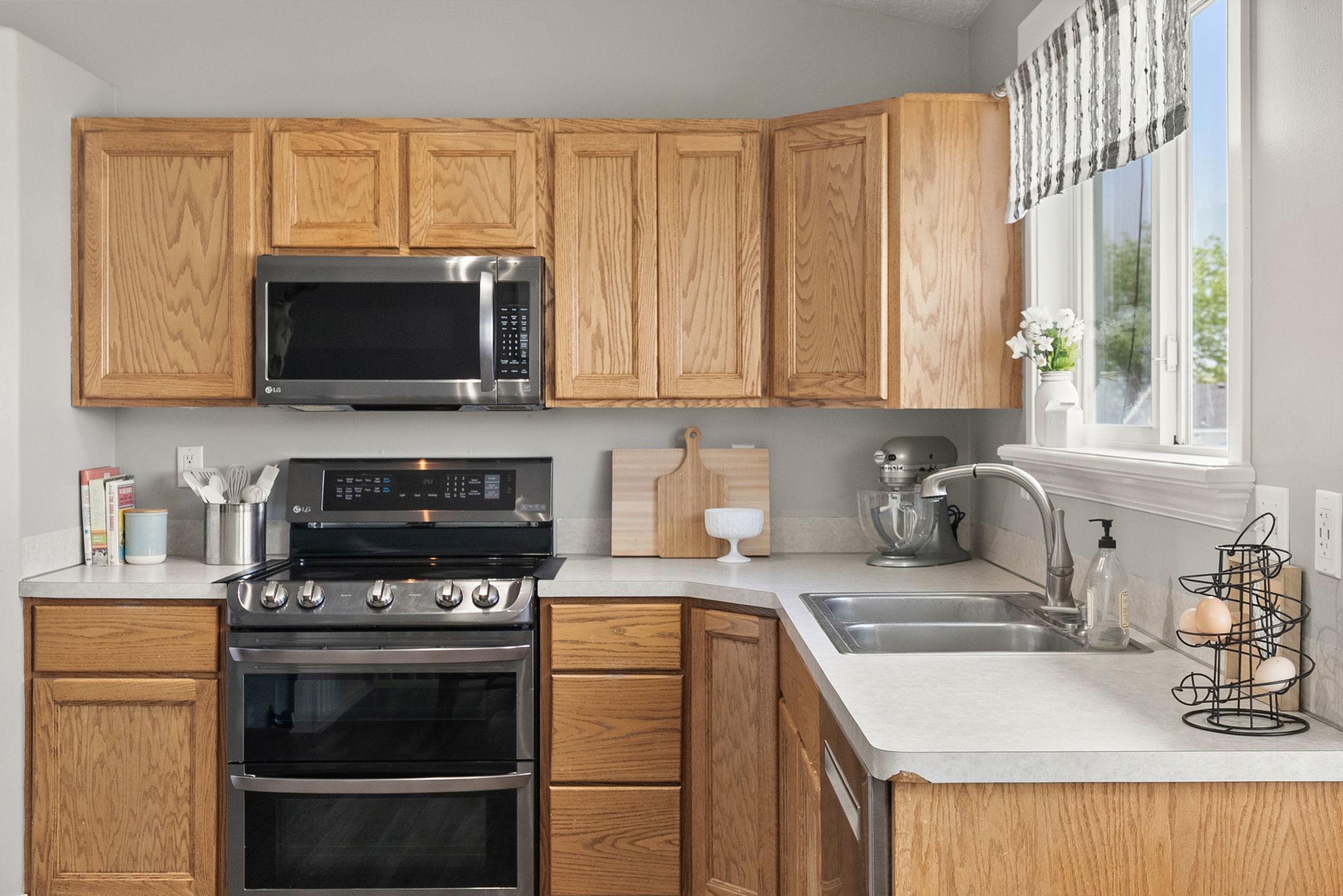 Kitchen featuring light wood cabinetry, light-toned countertops, a stainless steel double basin sink with an arched faucet, and a window with natural light