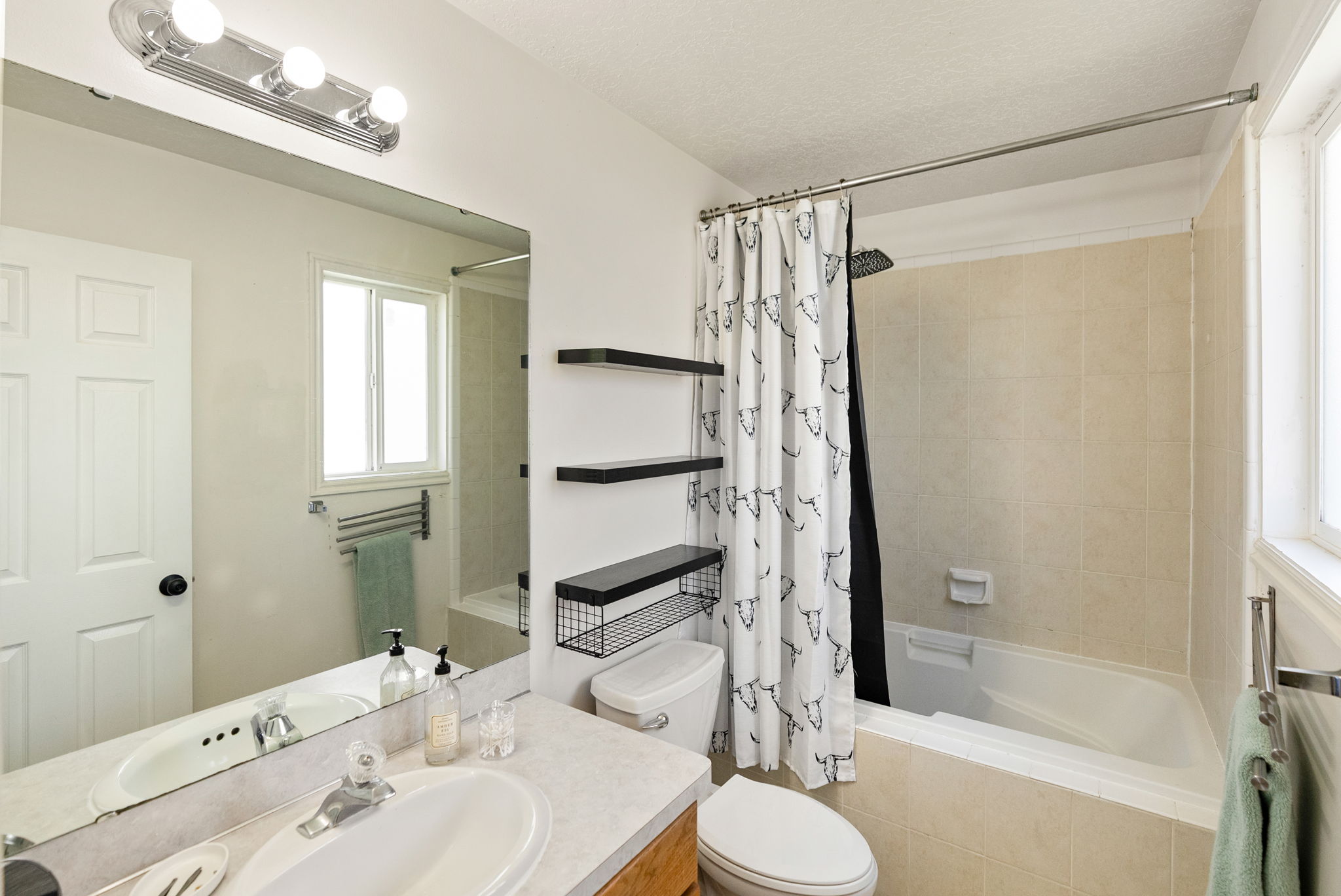 Bathroom featuring a combination shower and tub with ceramic tile surround, a single vanity with a laminate countertop, and a wall-mounted mirror