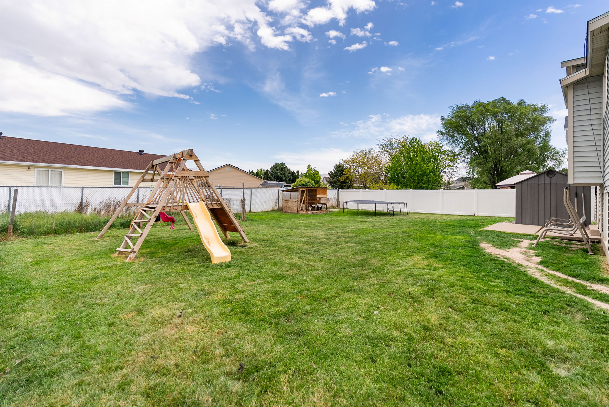 Expansive backyard featuring a manicured lawn, white vinyl fencing, a privacy fence, and a utility shed