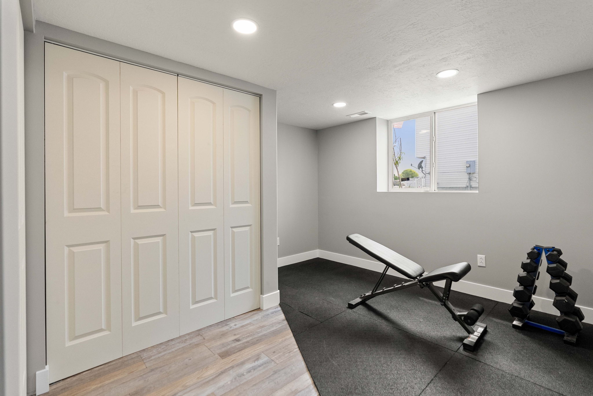 Recessed lighting illuminates this versatile space featuring light-toned wood-finish flooring, a bi-fold closet with paneled doors, and a window providing exterior visibility