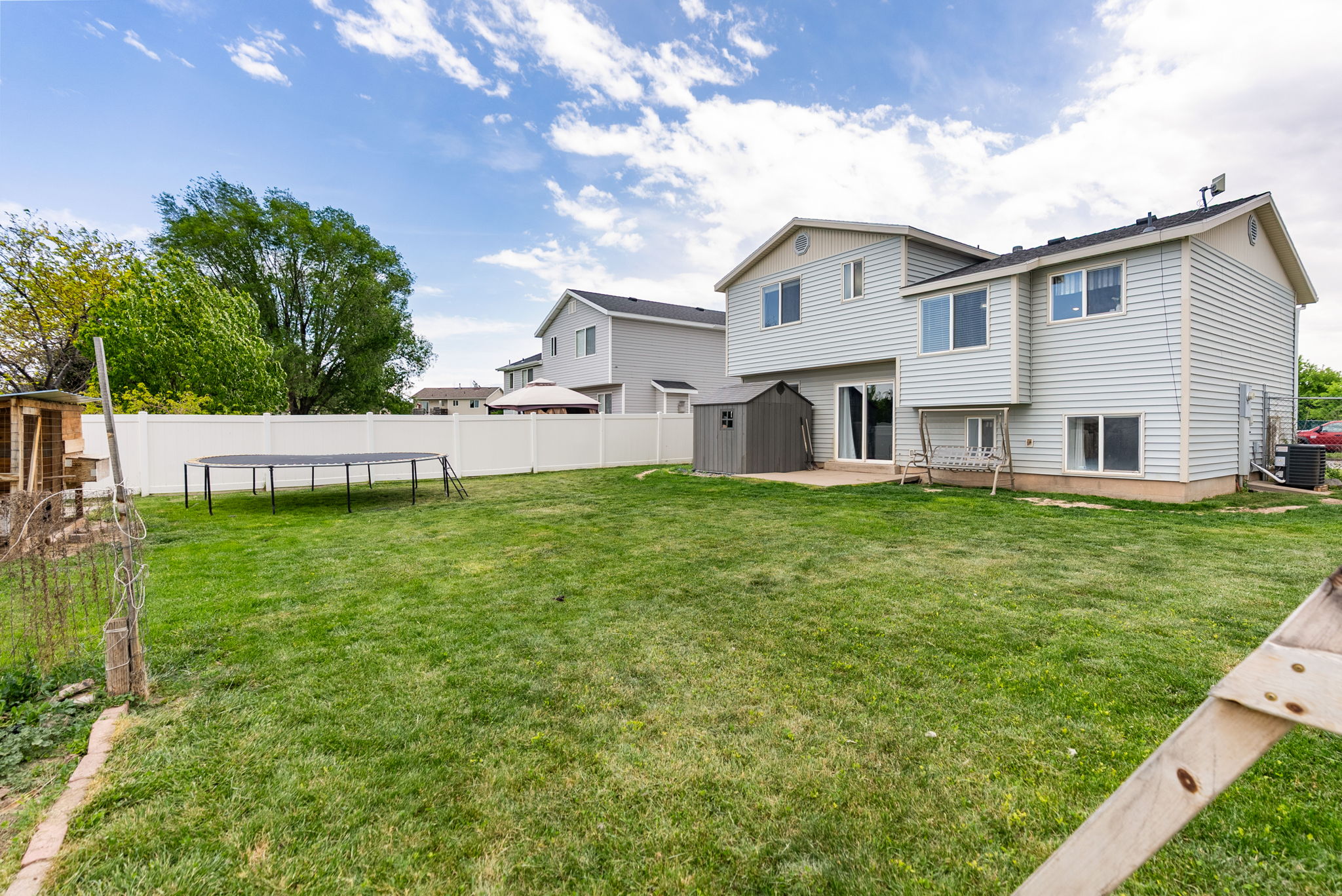 Expansive backyard featuring a manicured lawn, white vinyl privacy fencing, and a concrete patio