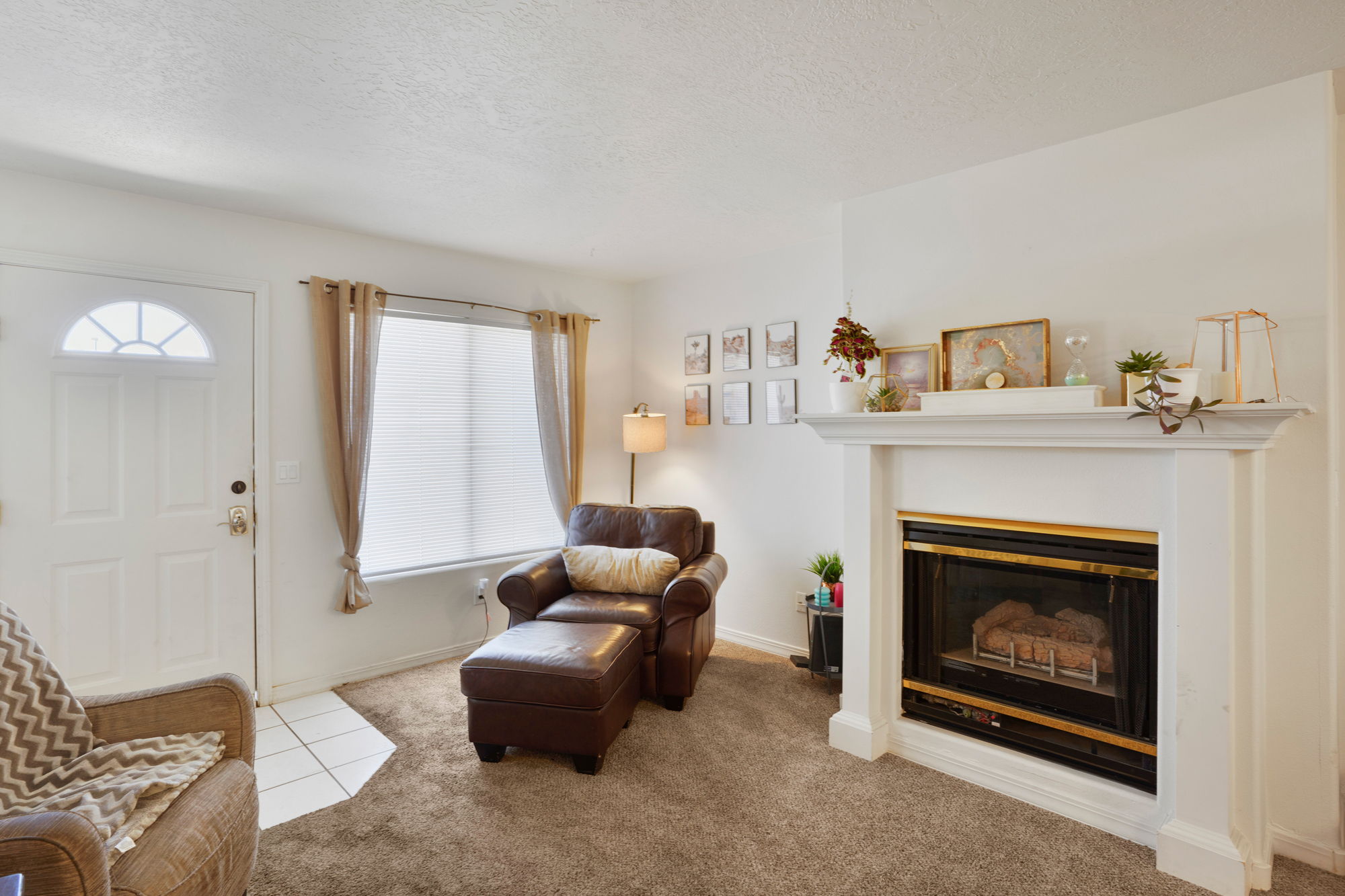 Living area featuring a white paneled entry door with a decorative transom, a large window with privacy blinds, and a white fireplace with a mantel