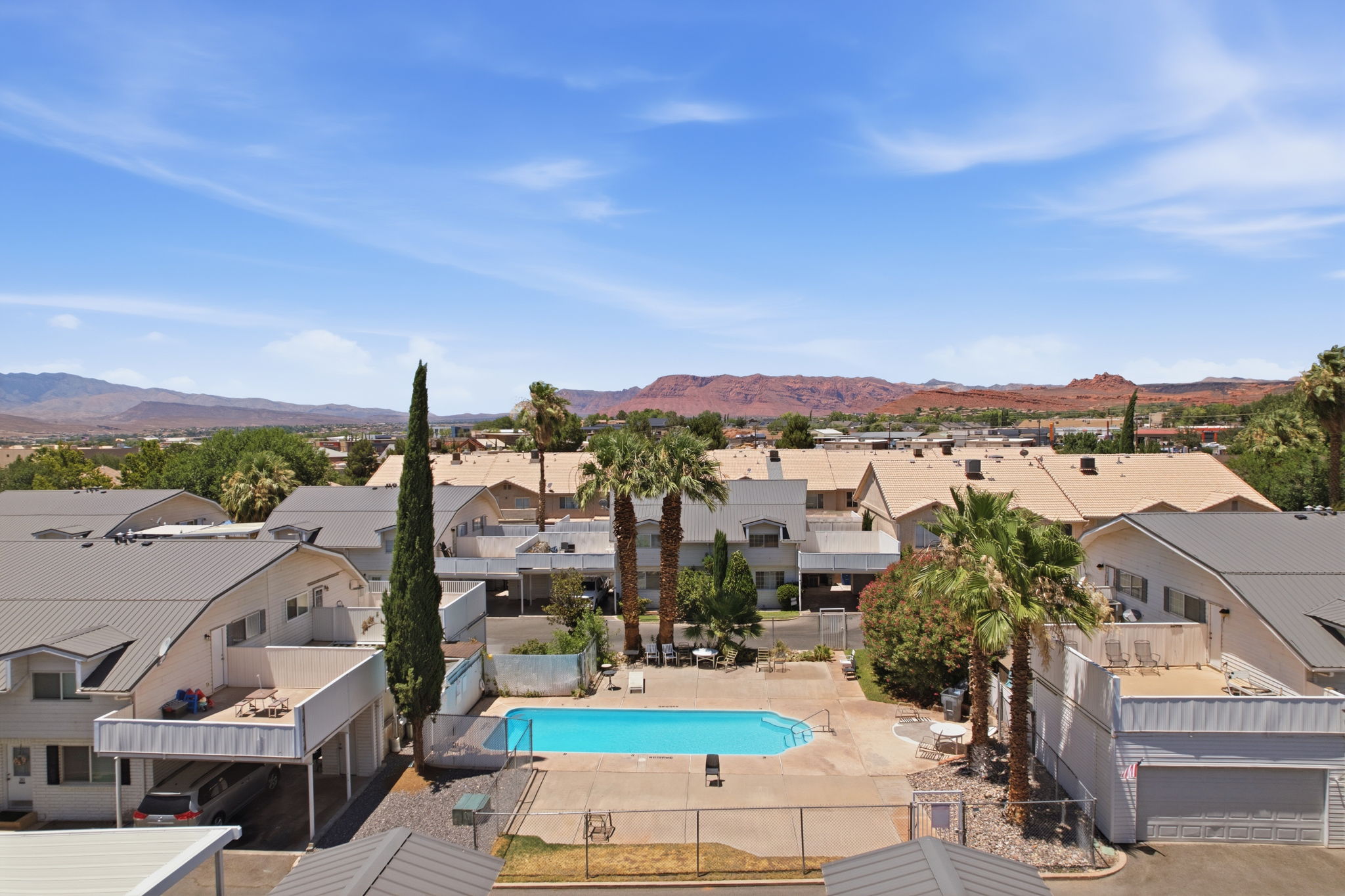Central swimming pool with surrounding concrete decking, fenced perimeter, and nearby palm trees
