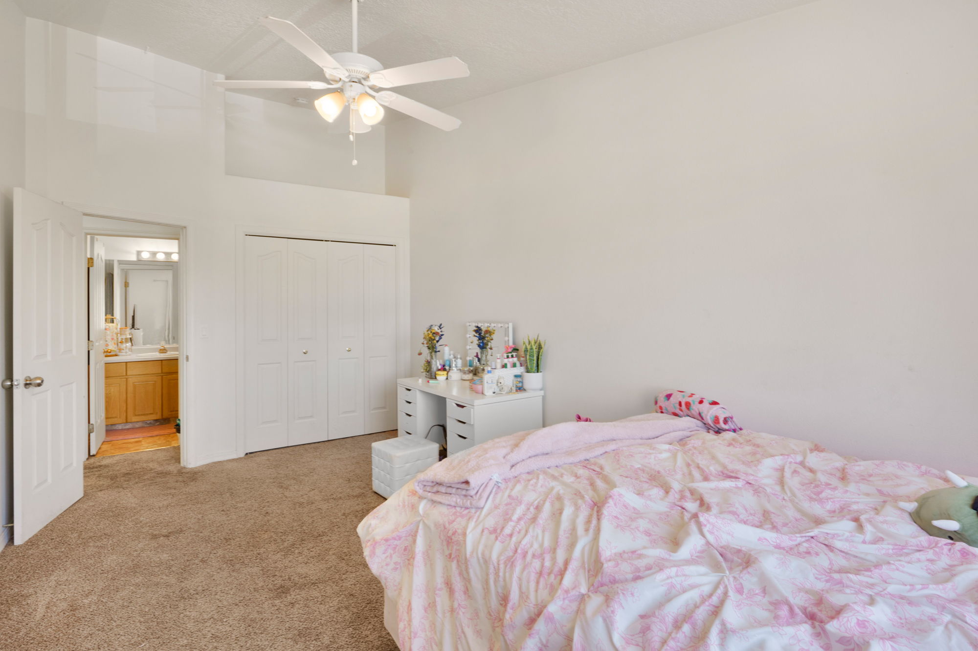 Carpeted room featuring a vaulted ceiling with a ceiling fan, bi-fold closet doors, and access to a bathroom with a vanity and mirror
