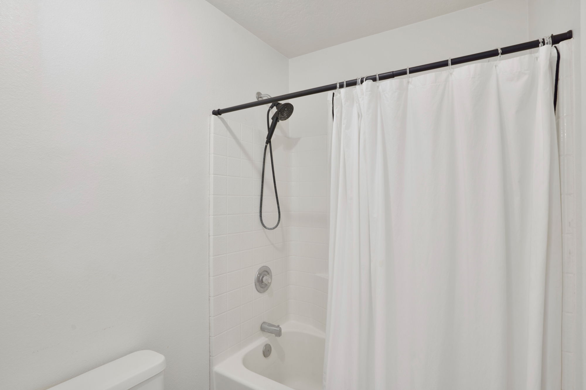 Shower-over-tub combination with white subway tile surround, matte black shower head, and coordinating shower rod