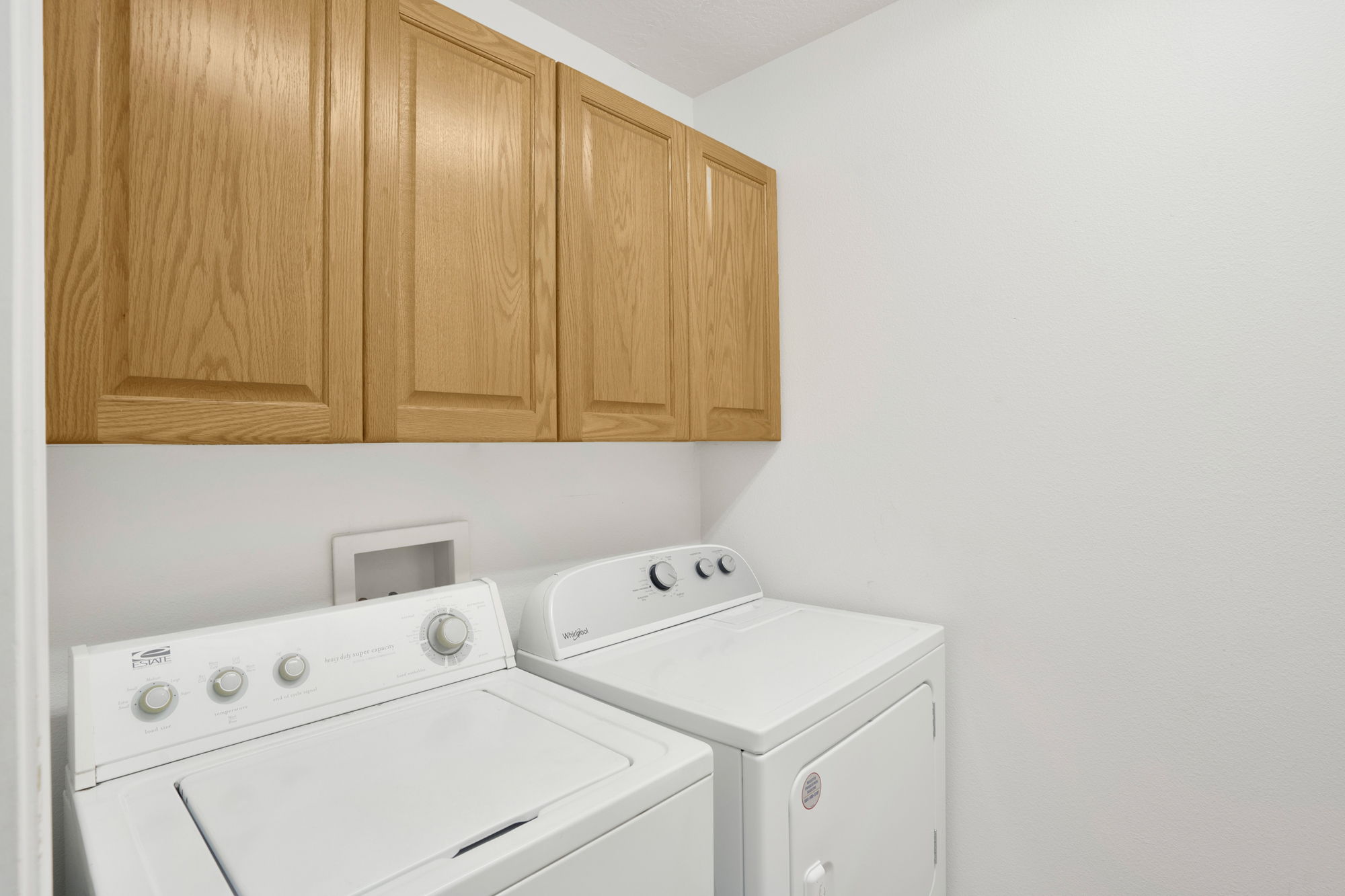 Laundry area featuring upper cabinetry with wood-finish doors, white walls, and a dedicated appliance space