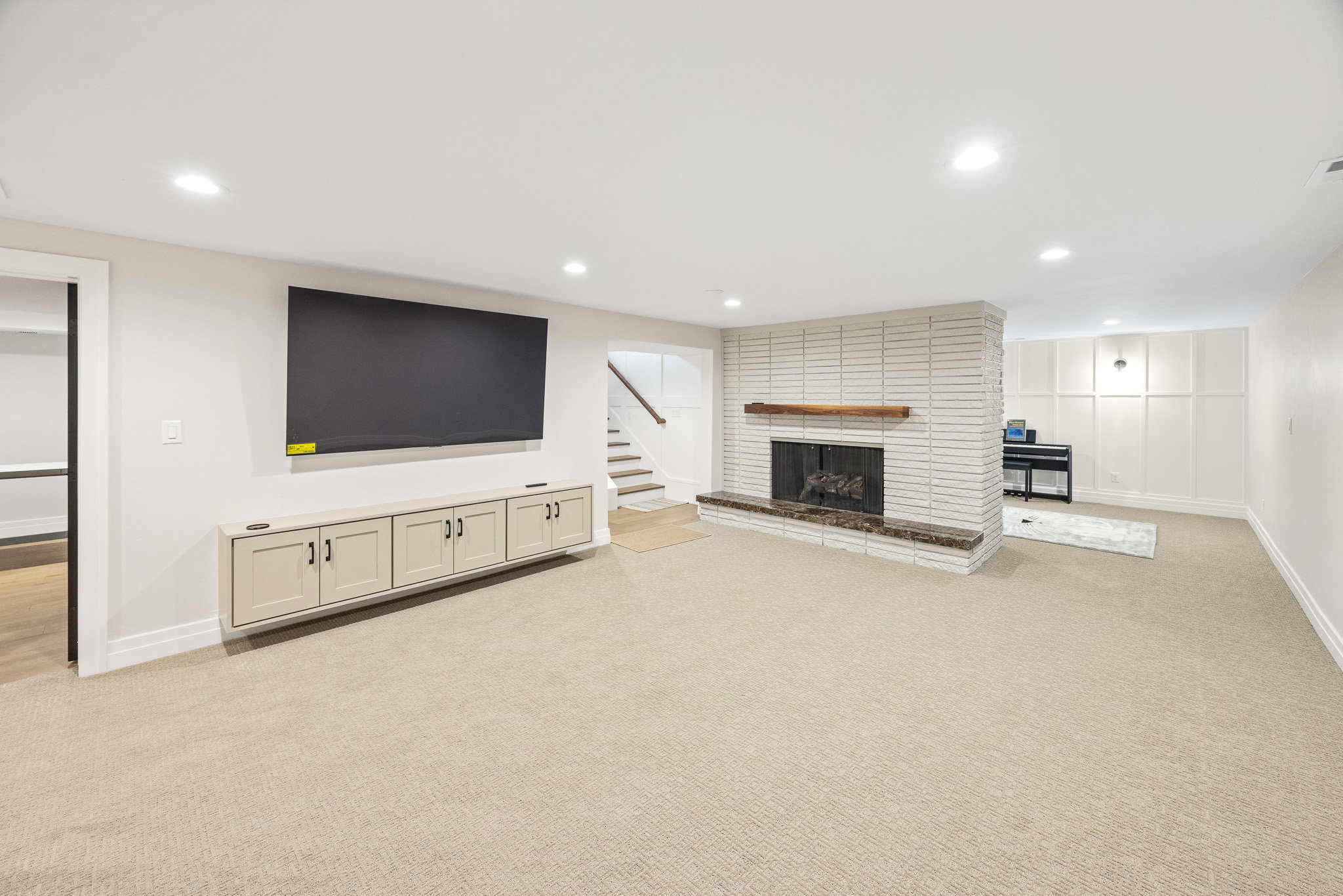 Spacious room featuring a white brick fireplace with a wood mantel, an integrated wall-mounted media cabinet, and light-toned carpeting throughout