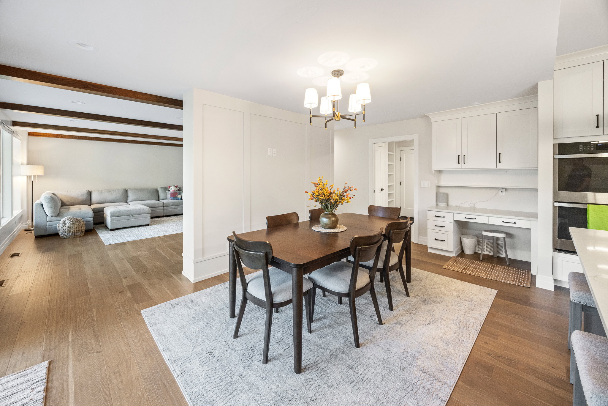 Open concept dining area featuring wood-finish flooring, a modern chandelier, and an integrated desk area with white cabinetry