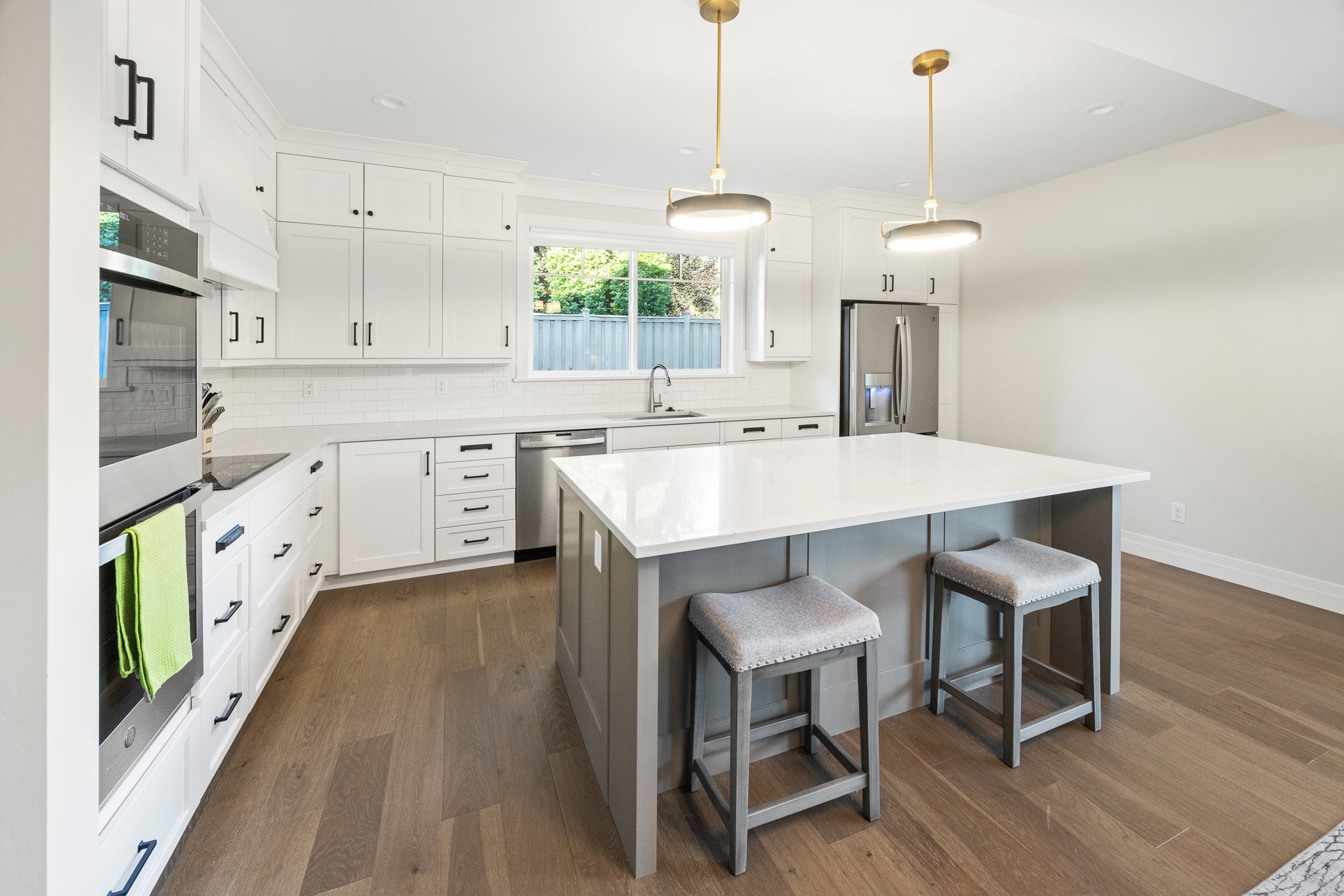 Modern kitchen featuring white cabinetry with black hardware, stainless steel appliances, and wood-finish flooring