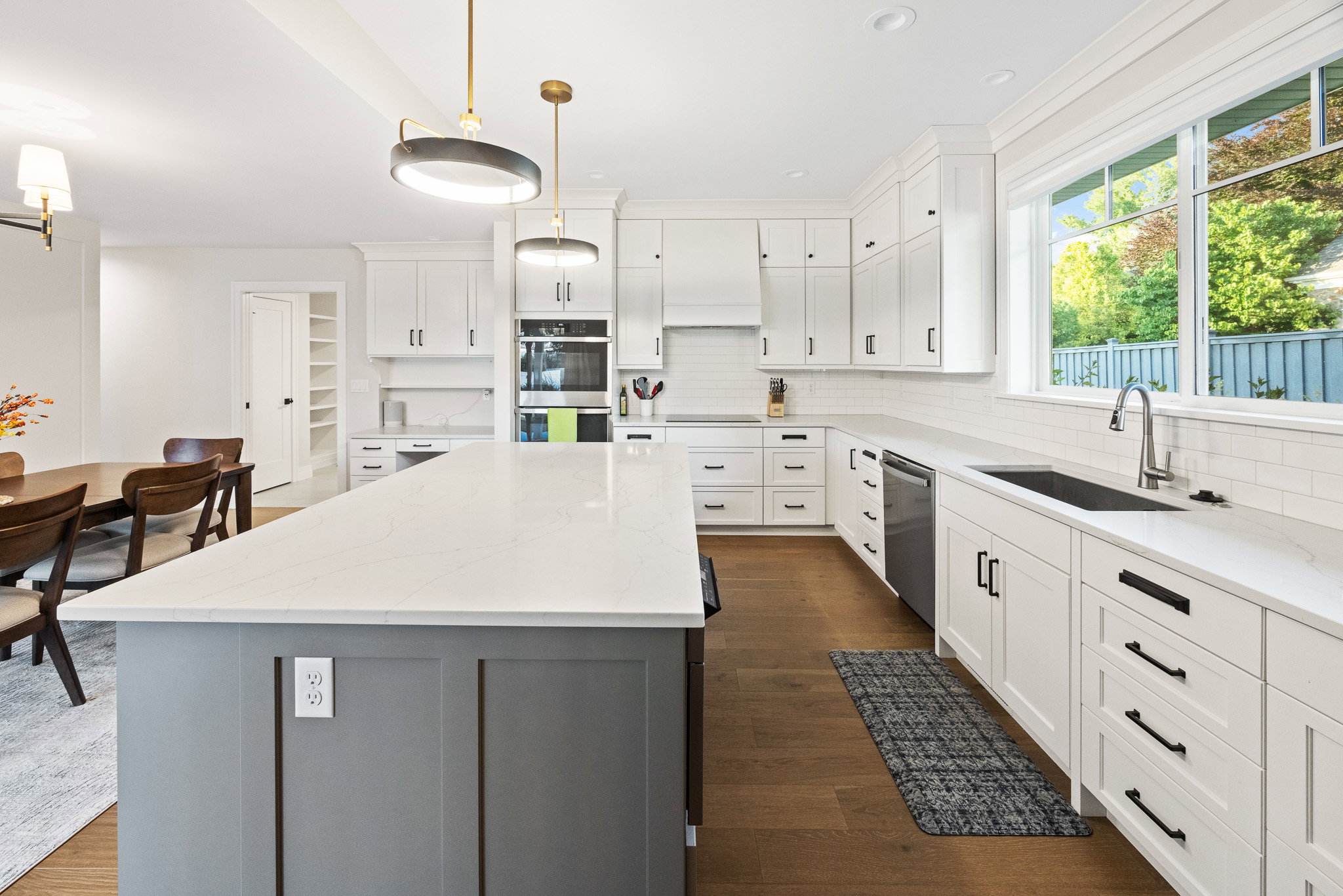 Modern kitchen featuring a large central island with a light-toned countertop, white cabinetry with dark hardware, stainless steel appliances, a subway tile backsplash, and wood-finish flooring