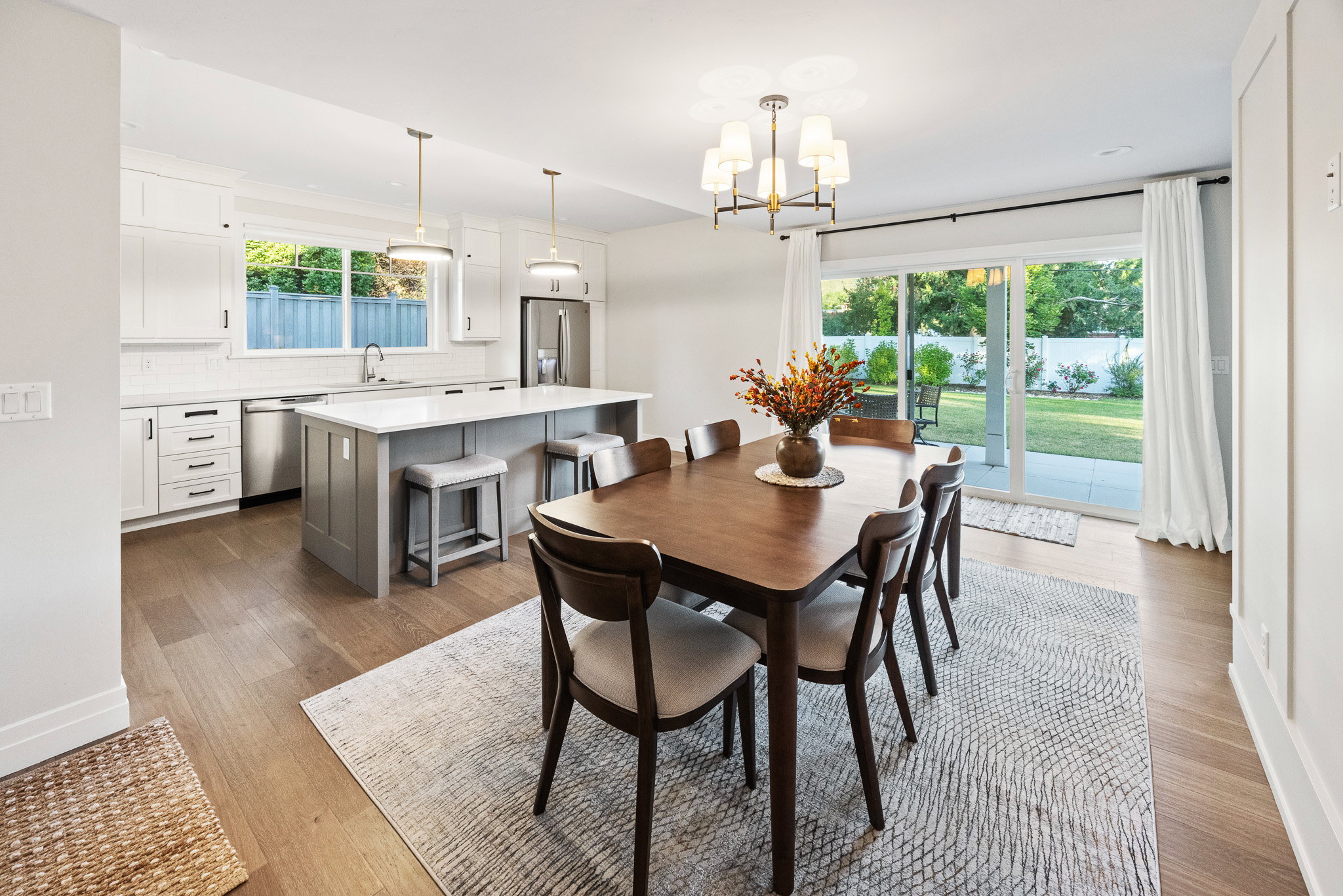 Open-concept kitchen and dining area featuring wood-finish flooring, white cabinetry, a kitchen island with seating, stainless steel appliances, and sliding glass doors opening to the backyard
