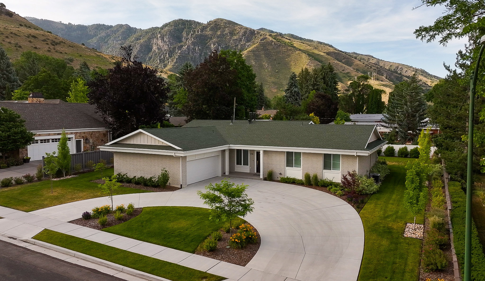 Ranch-style residence featuring an attached two-car garage, a circular driveway, and a meticulously landscaped front yard with mature shrubbery